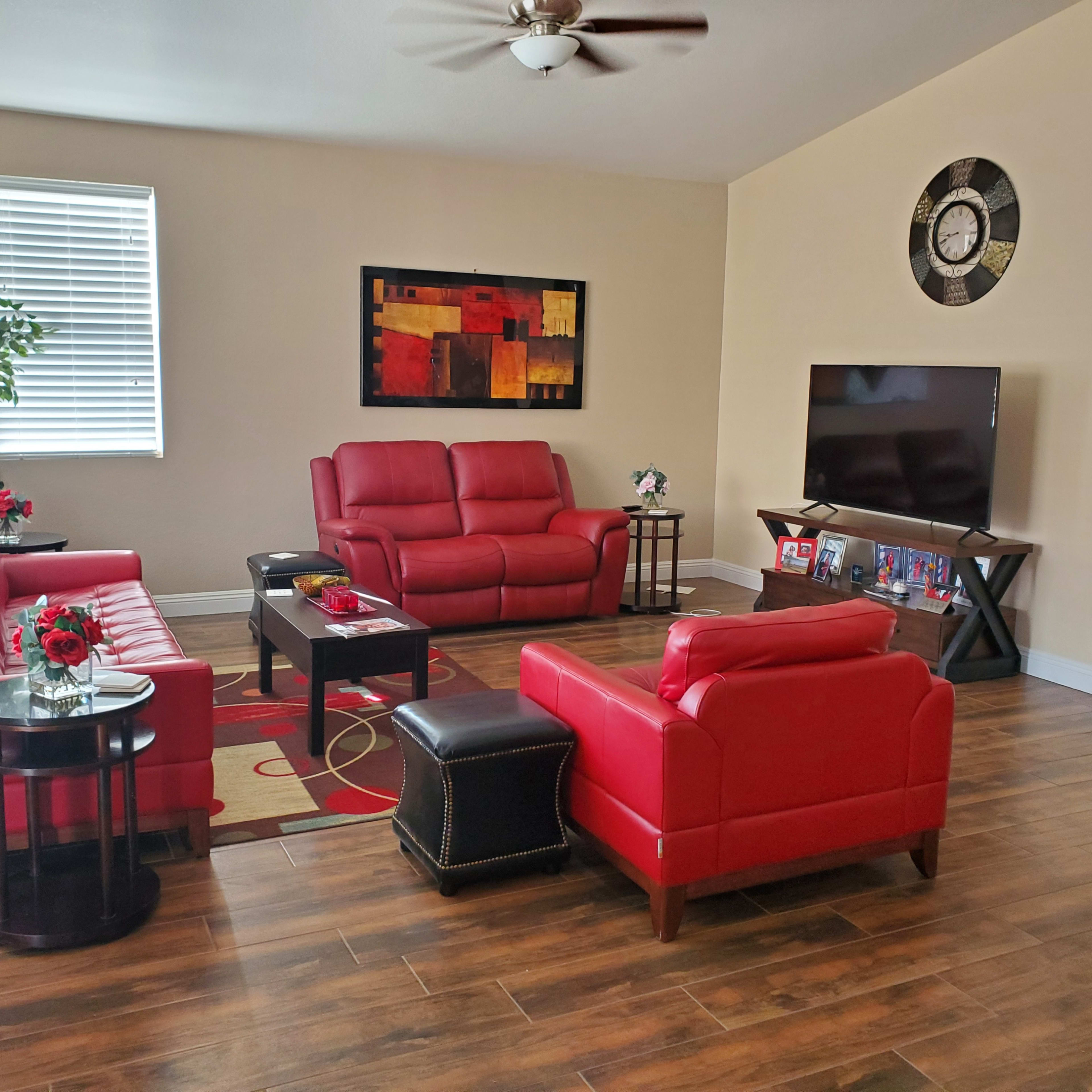 The living room features red leather sofas, a black coffee table, a large television on an entertainment unit, and wall art in a modern style.