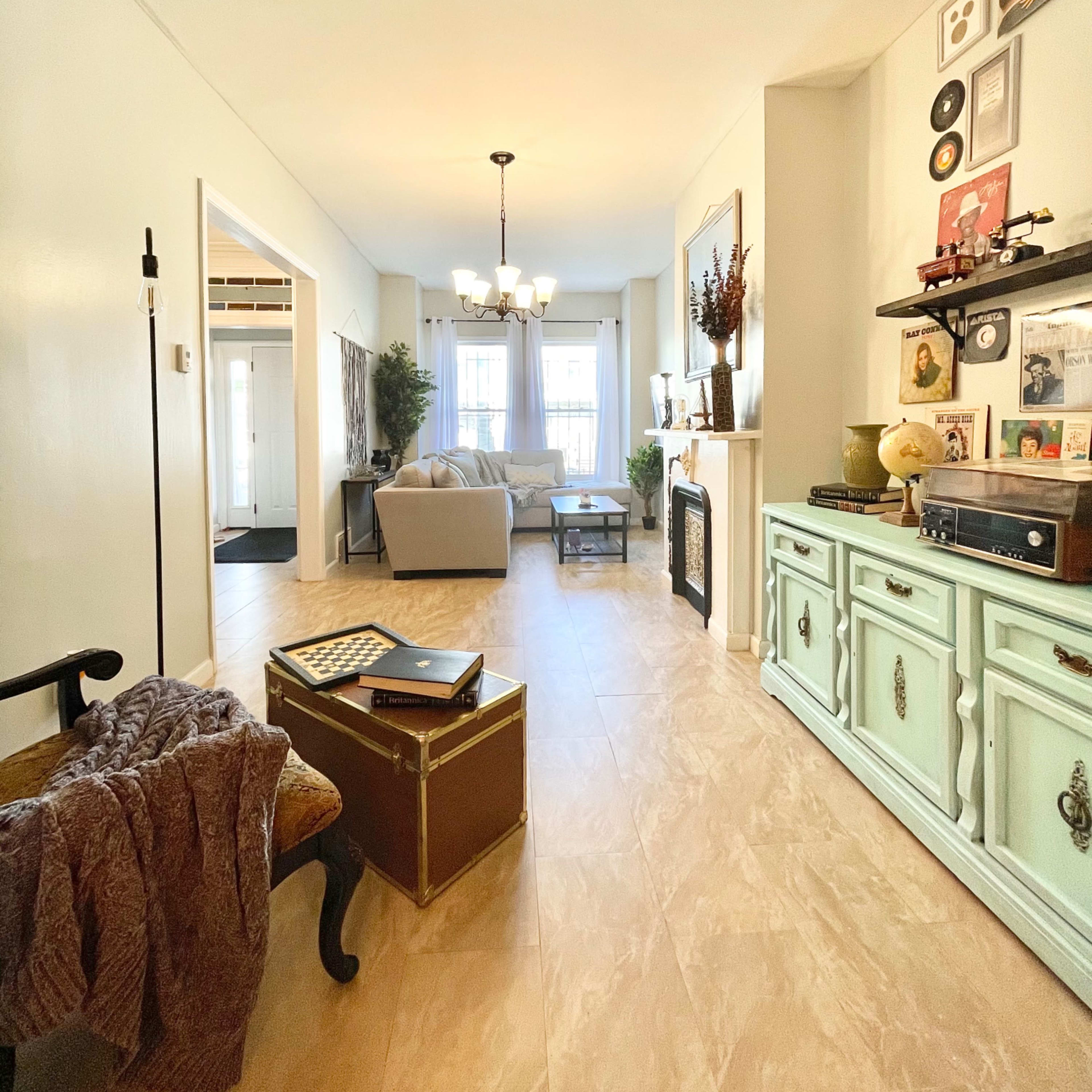 A well-lit living room with a beige sofa, a coffee table, and decorative items on a pale green console.