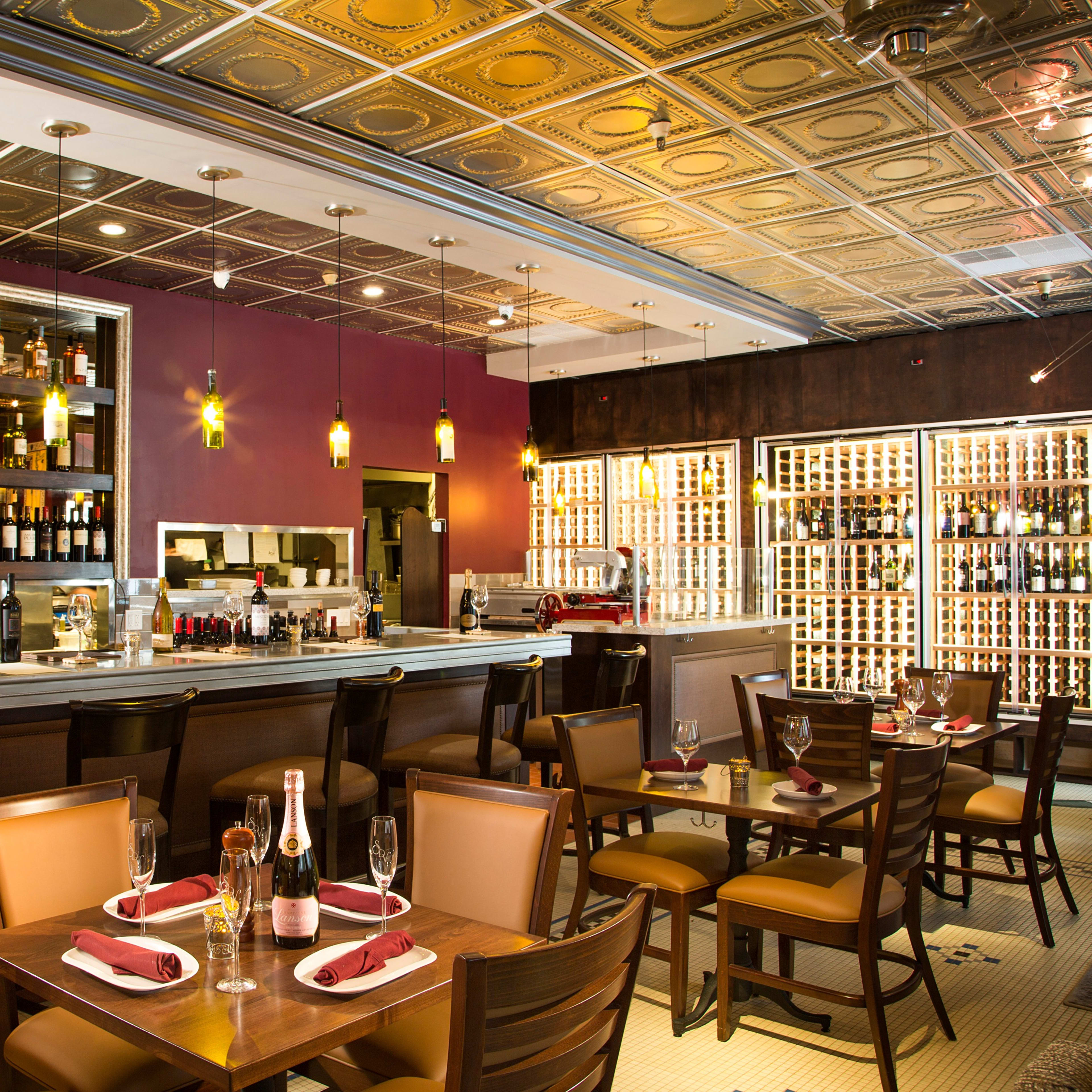 A restaurant interior featuring a stylish bar with shelves of wine and several tables set for dining.