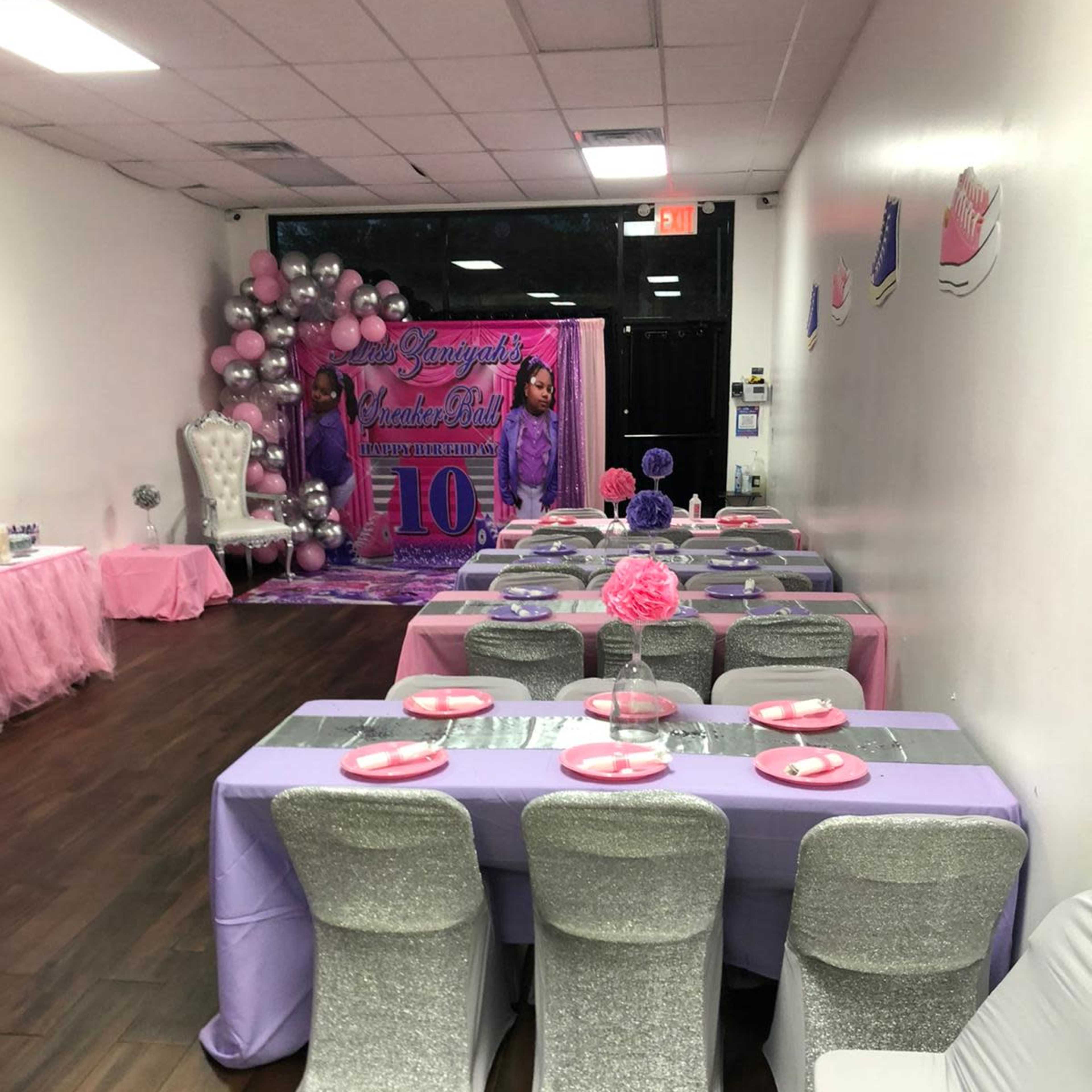 A decorated party venue with tables set in purple and silver, featuring a backdrop for a 10th birthday celebration.