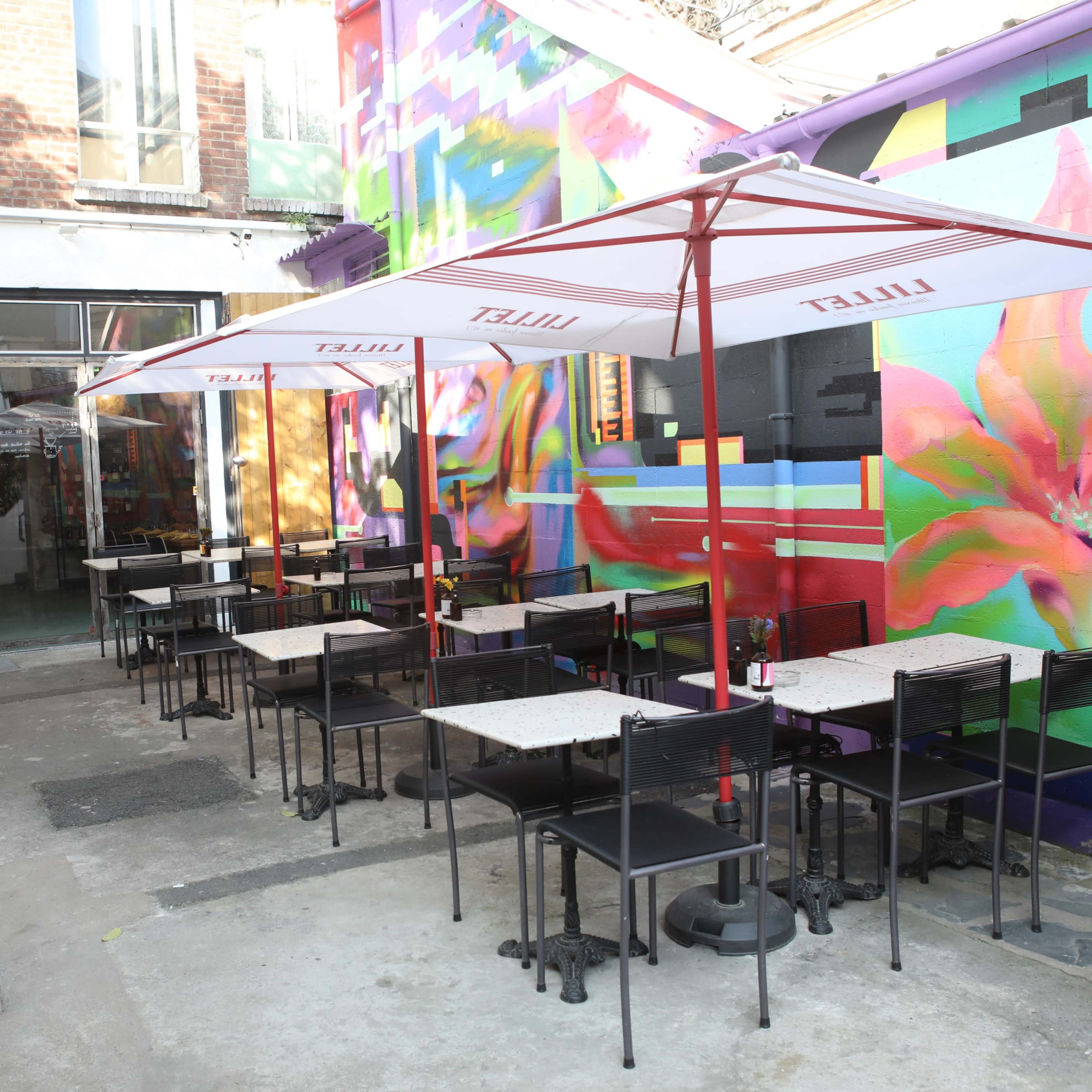 A vibrant outdoor seating area features tables and umbrellas in front of a colorful wall mural.