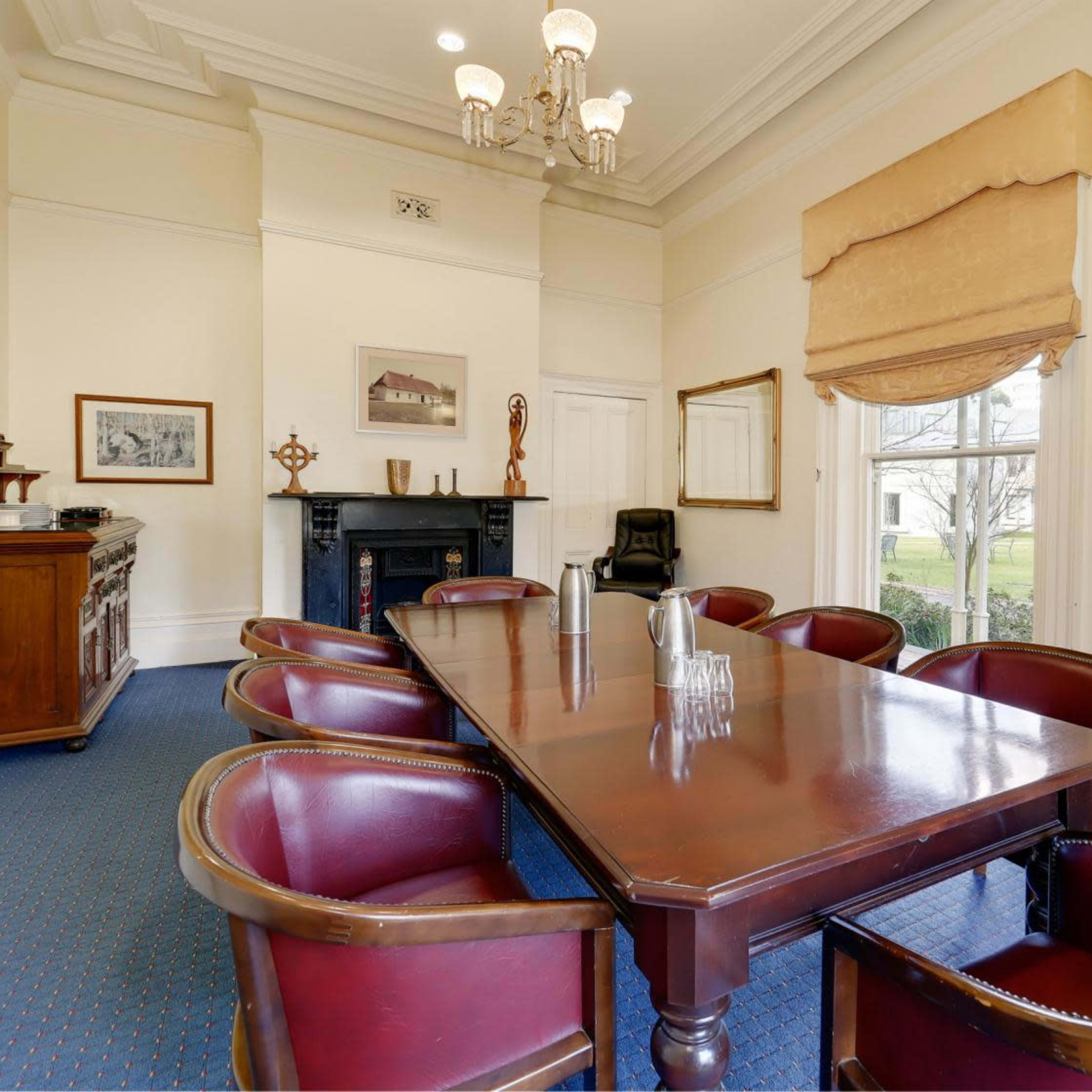 A dining room features a large wooden table surrounded by dark leather chairs, with a sideboard and a decorative mirror on the walls.
