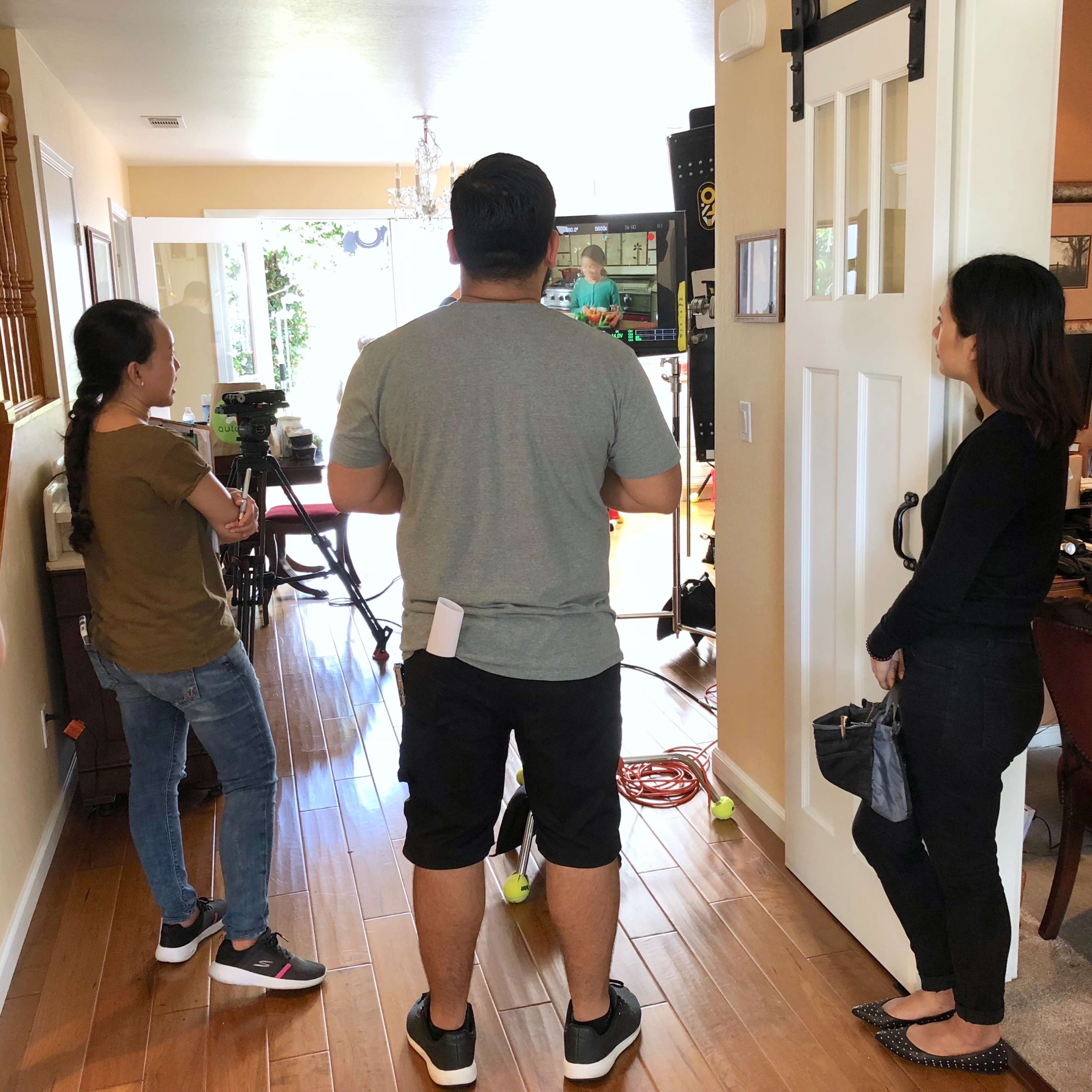 A group of four people stands in a well-lit room, observing a production setup with cameras and equipment.