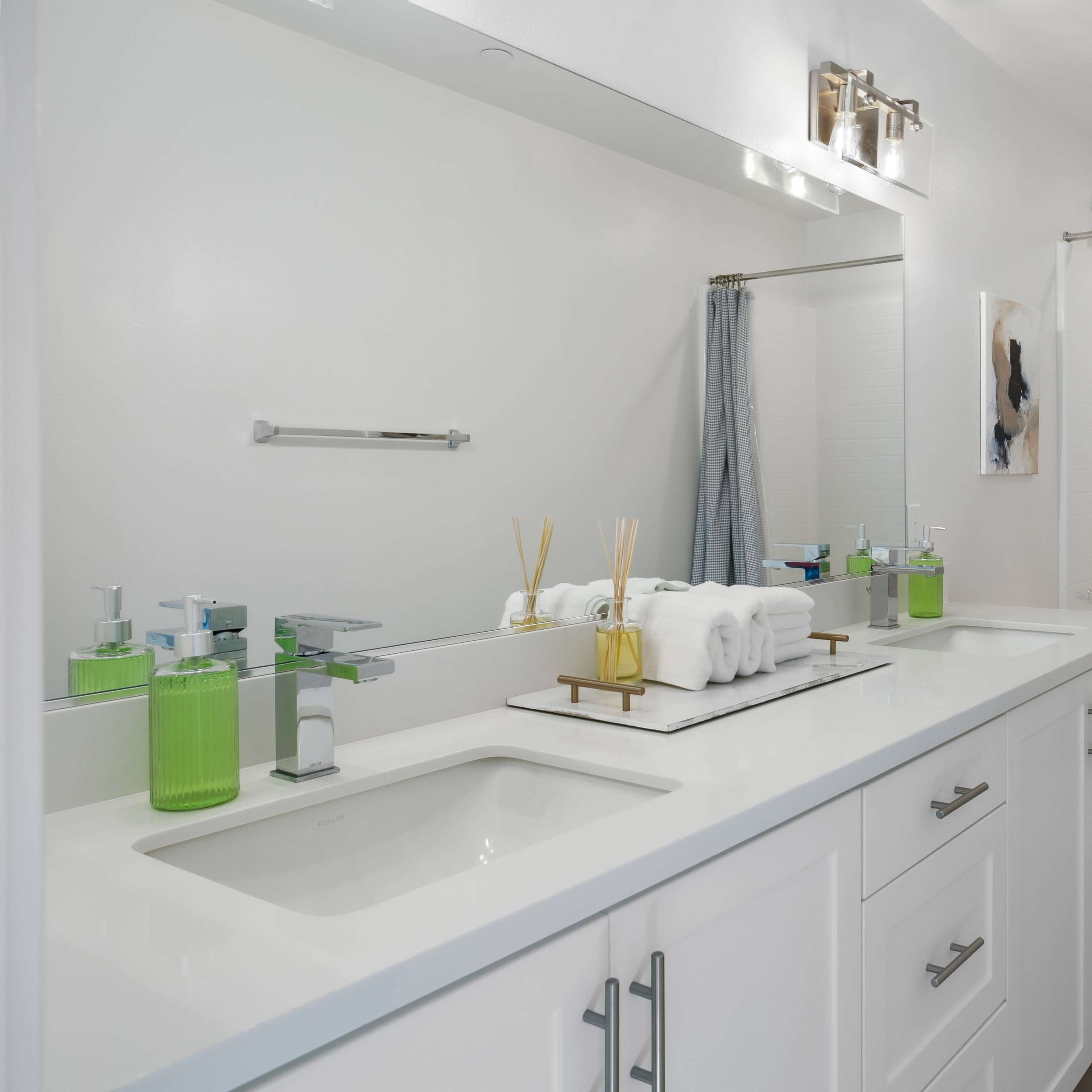 A modern bathroom with a double vanity, green toiletries, a white bathtub, and a shower with a gray curtain.