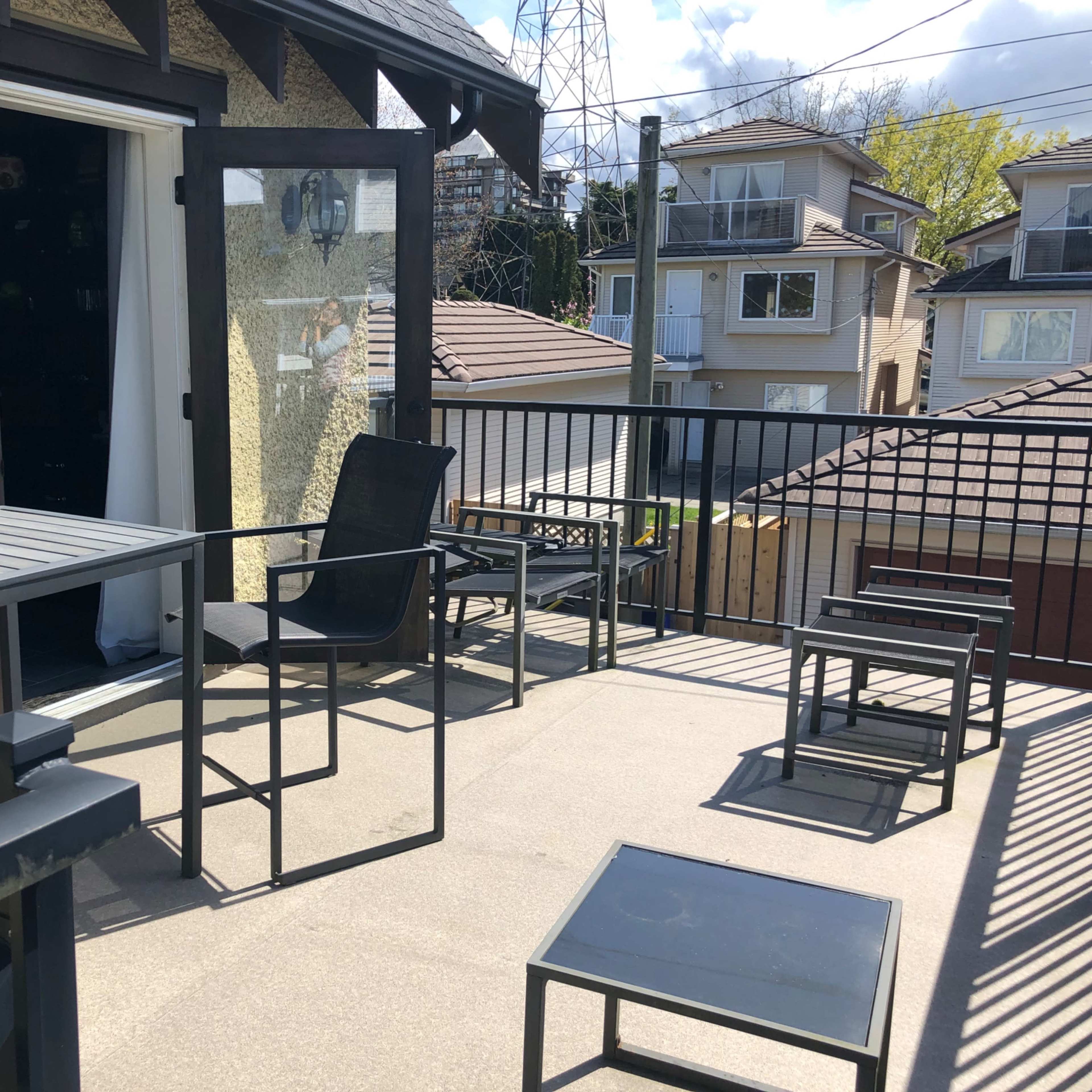 A rooftop terrace with several metal tables and chairs overlooking a residential area.