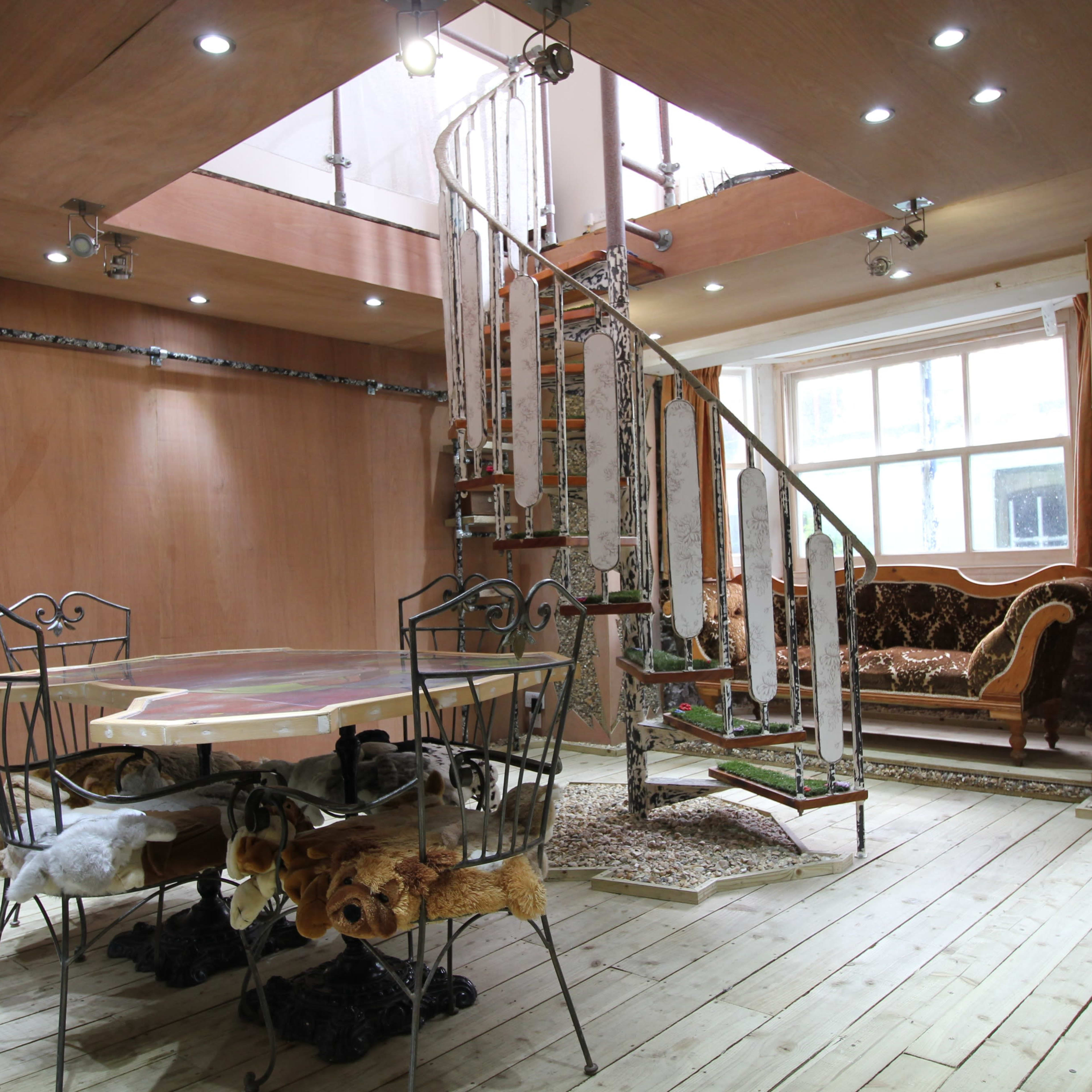 A unique interior space with wooden flooring, a spiral staircase, a circular dining table with chairs, and an assortment of decorative elements throughout the room.
