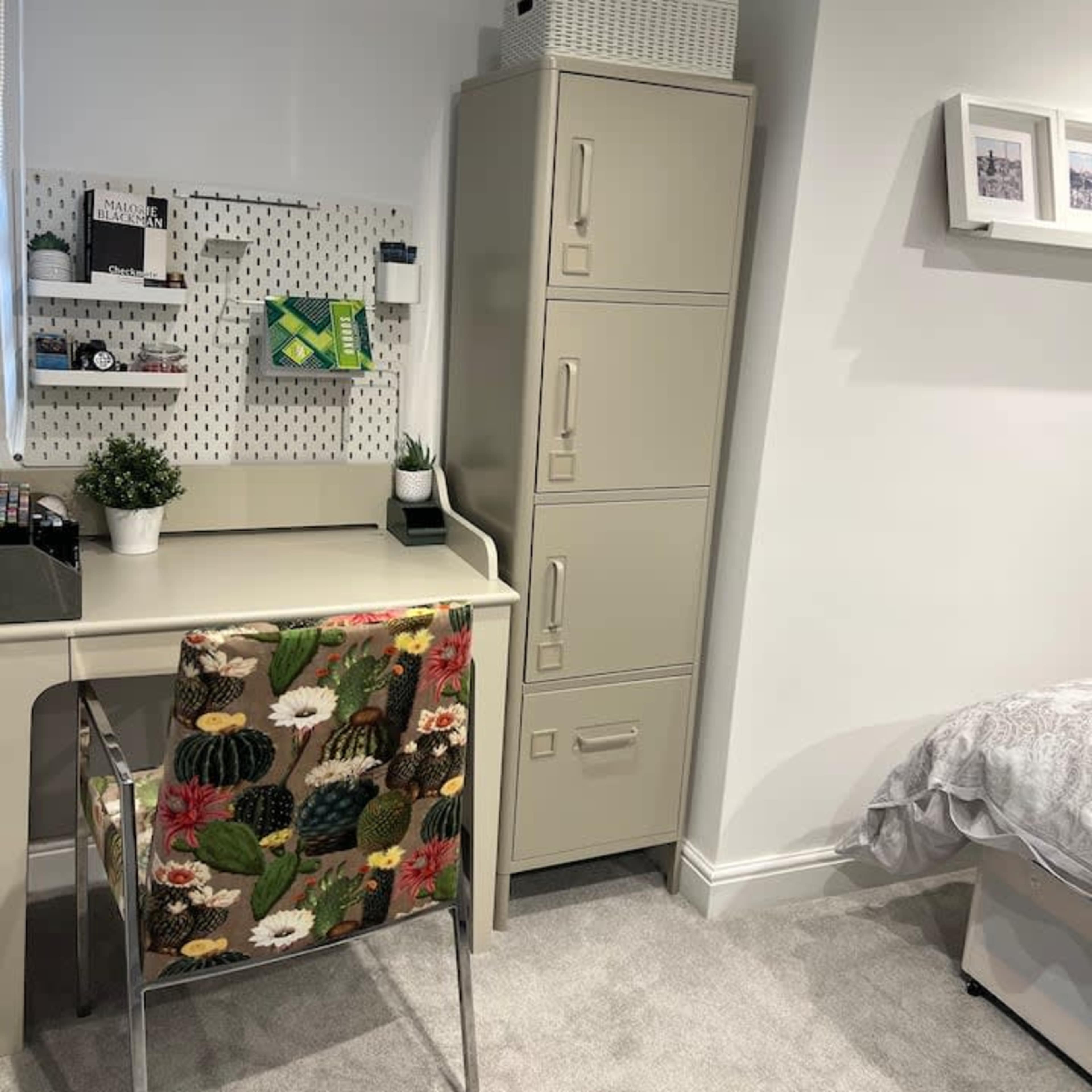 A small office space featuring a desk with a patterned chair, a storage cabinet, and a wall-mounted organizer with various items.