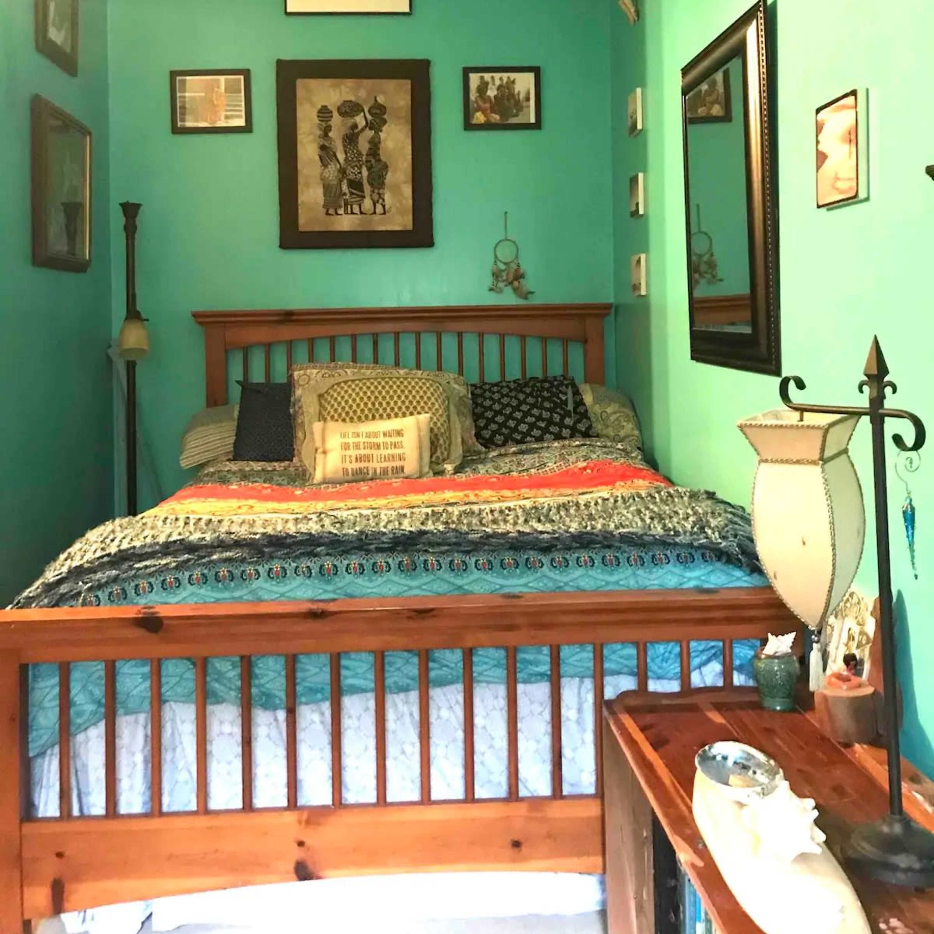 A small bedroom with a wooden bed, turquoise walls, and various framed pictures and decorative items arranged around the room.