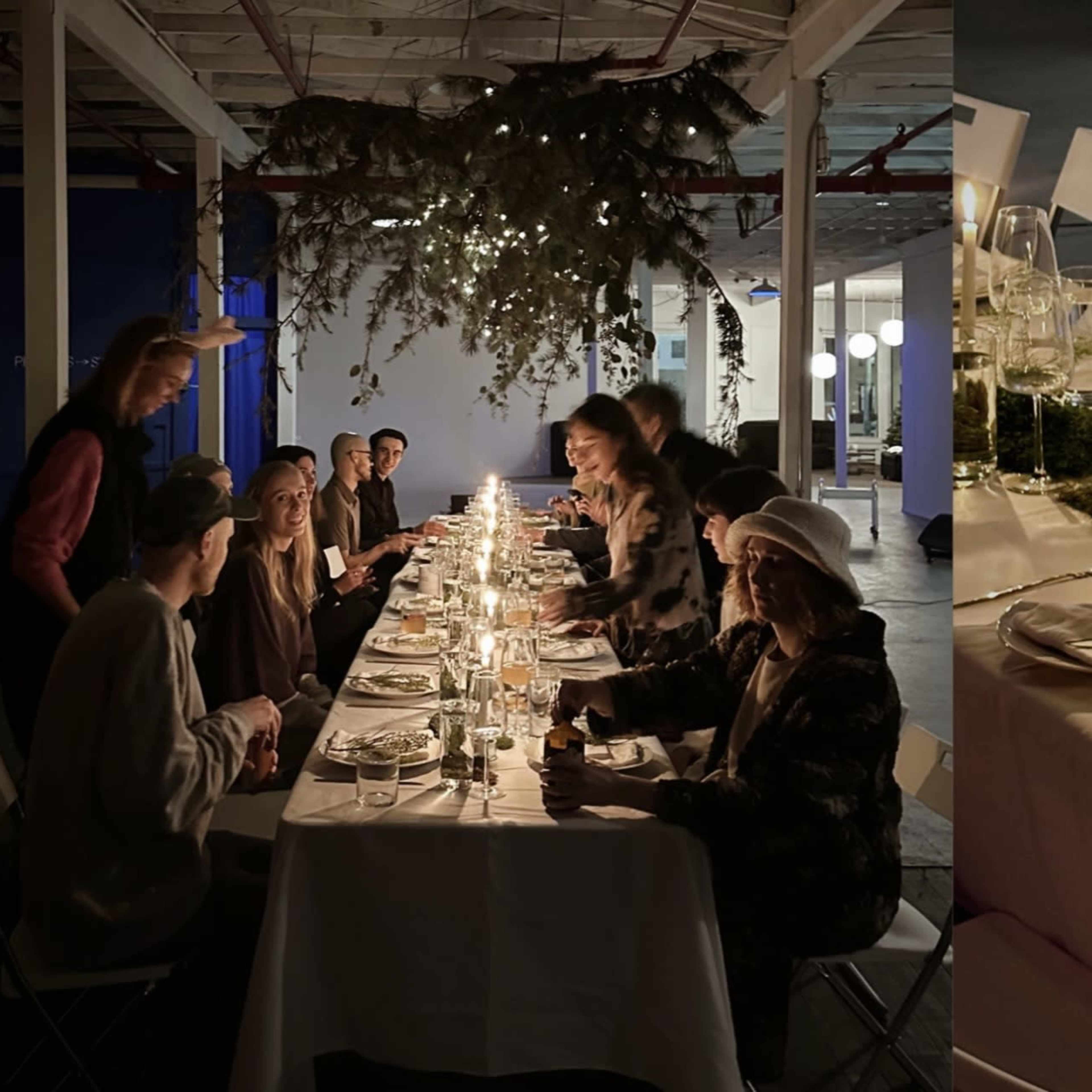 A long table is set with candles and greenery, surrounded by people dining in a decorated industrial space.