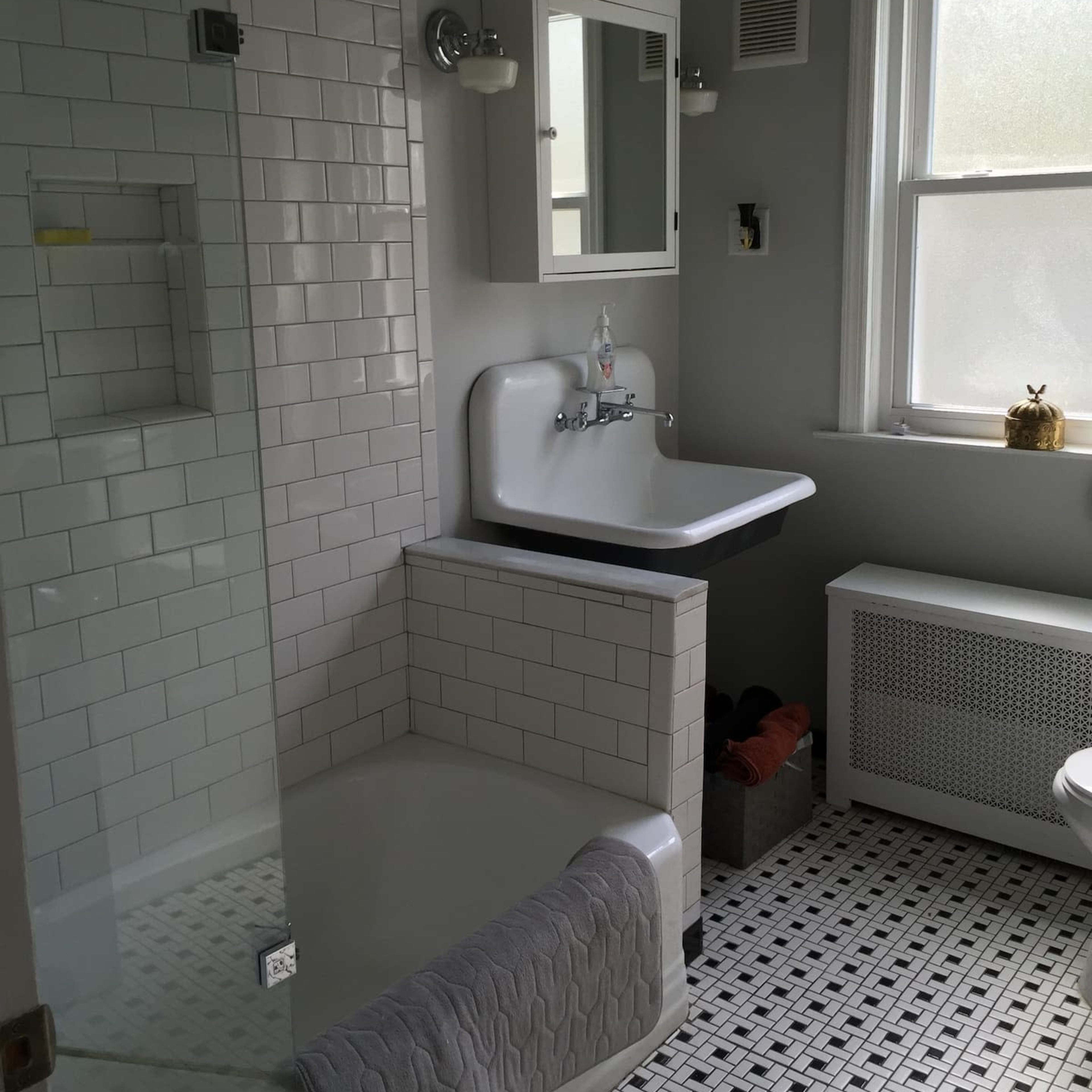 A modern bathroom featuring a glass shower enclosure, a white sink with a wall-mounted mirror, and a patterned tile floor.