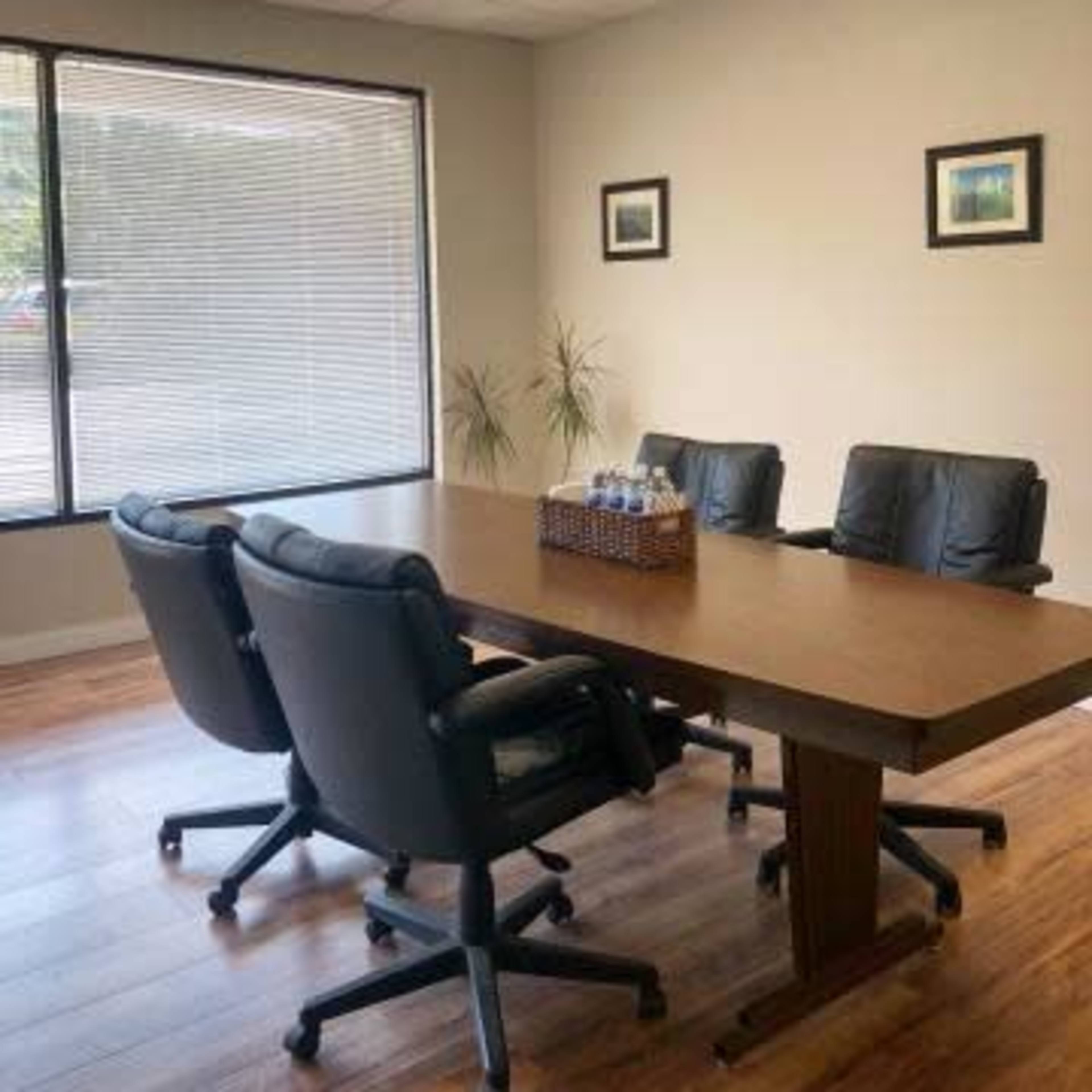 A conference room features a large wooden table surrounded by four leather chairs and a basket with water bottles on top.