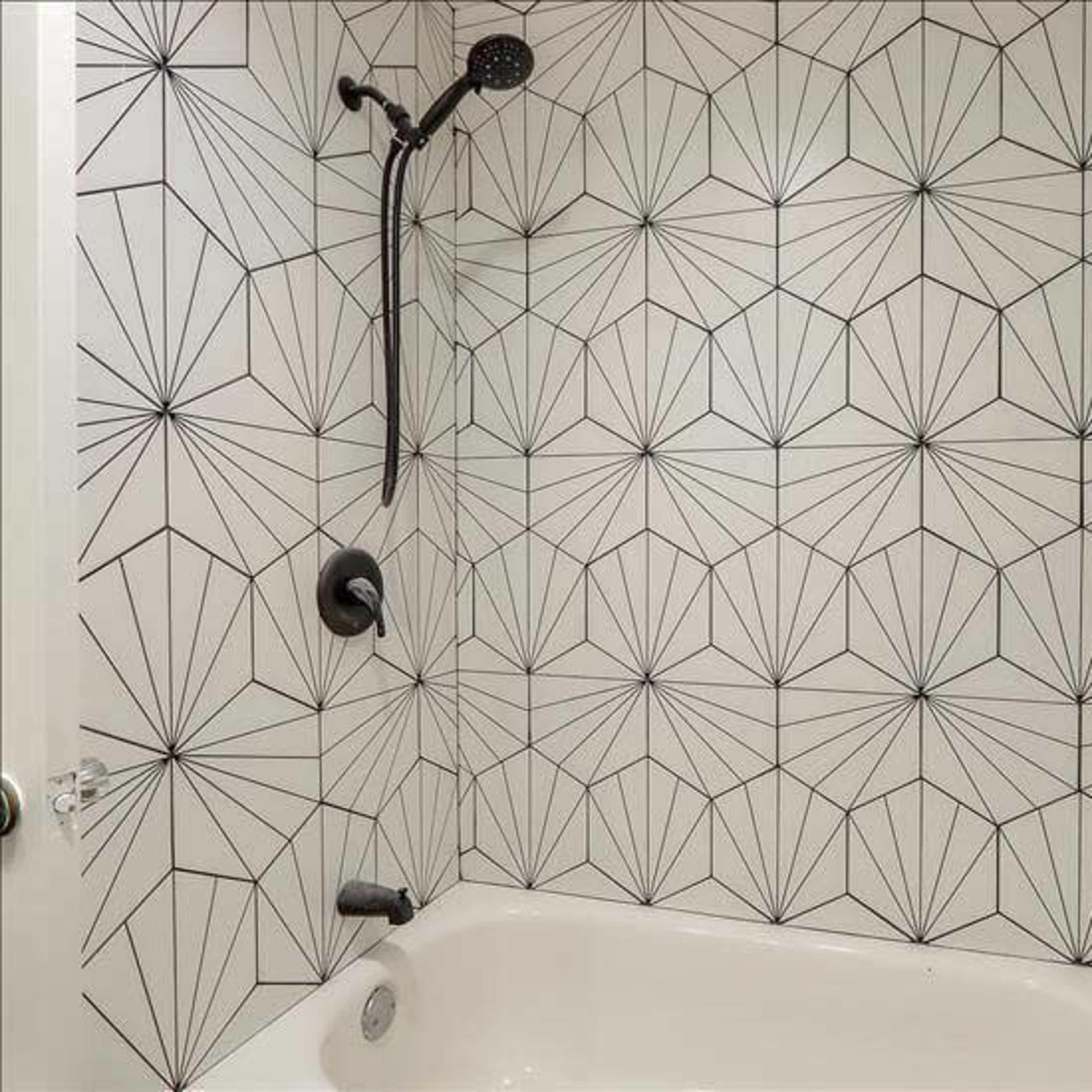 A modern shower space featuring geometric patterned tiles on the walls and a simple tub with a showerhead above.