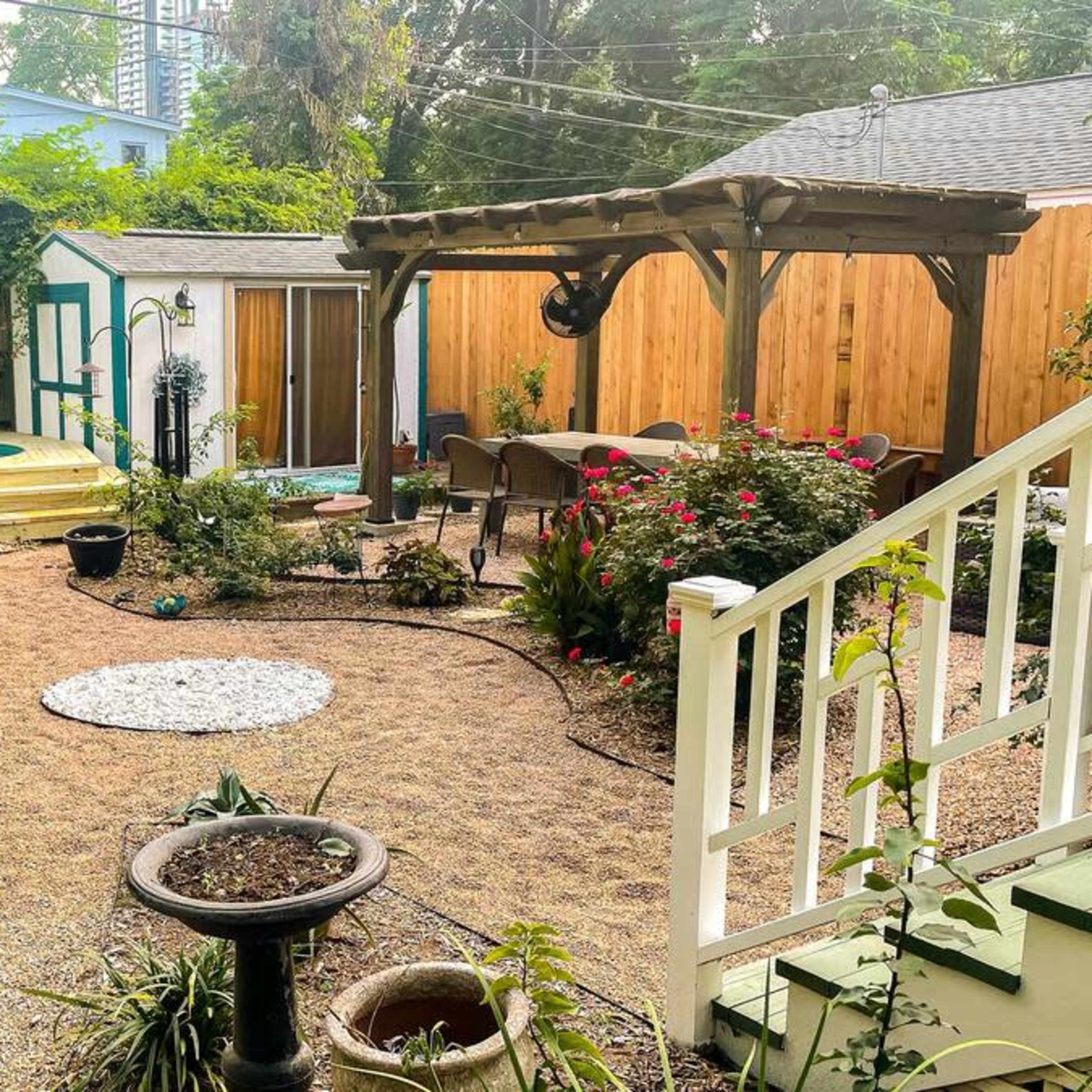 A landscaped backyard with a circular stone path, garden beds, a pergola, and a small wooden shed.