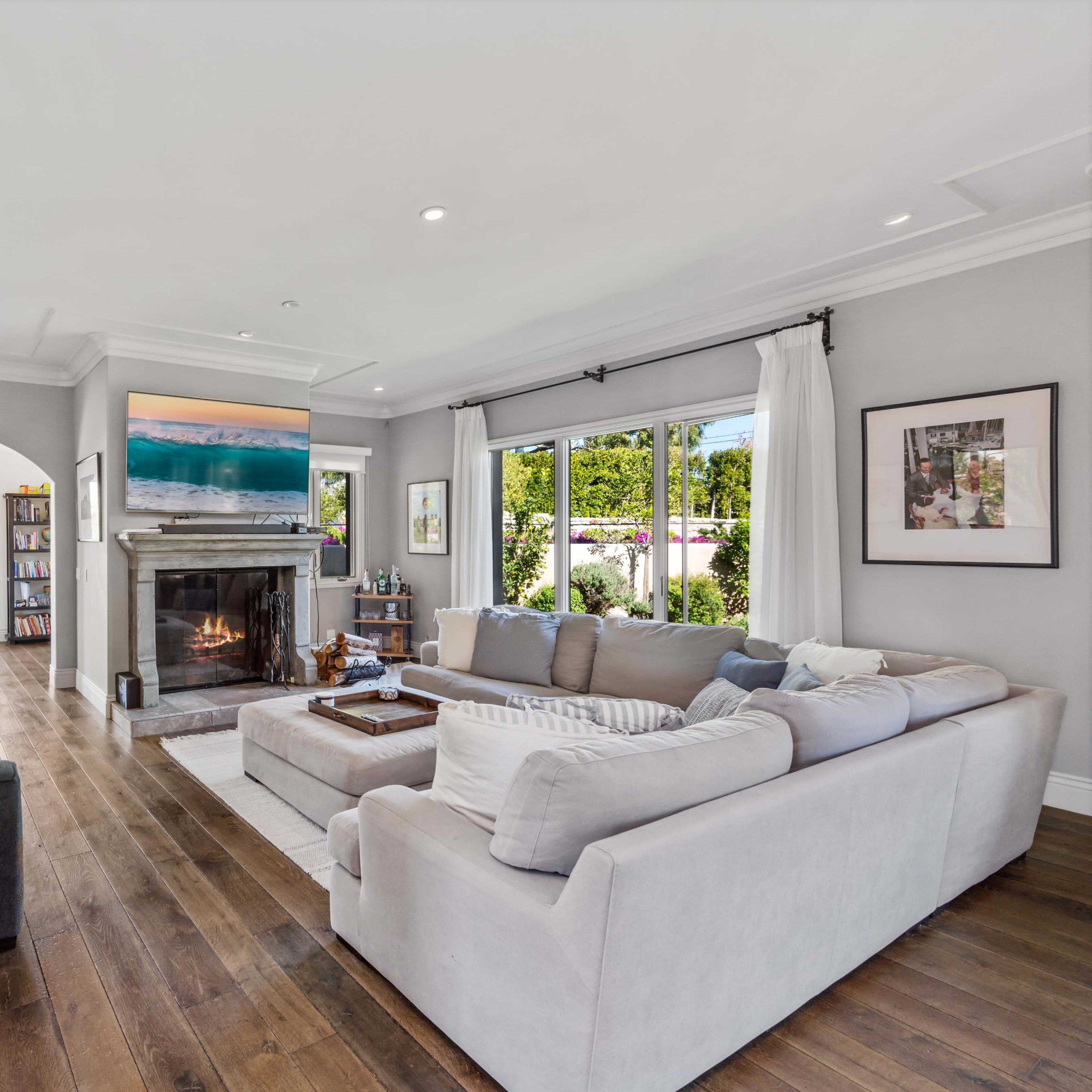 A modern living room with a large sectional sofa, a fireplace, and a view of the outdoor garden through glass doors.
