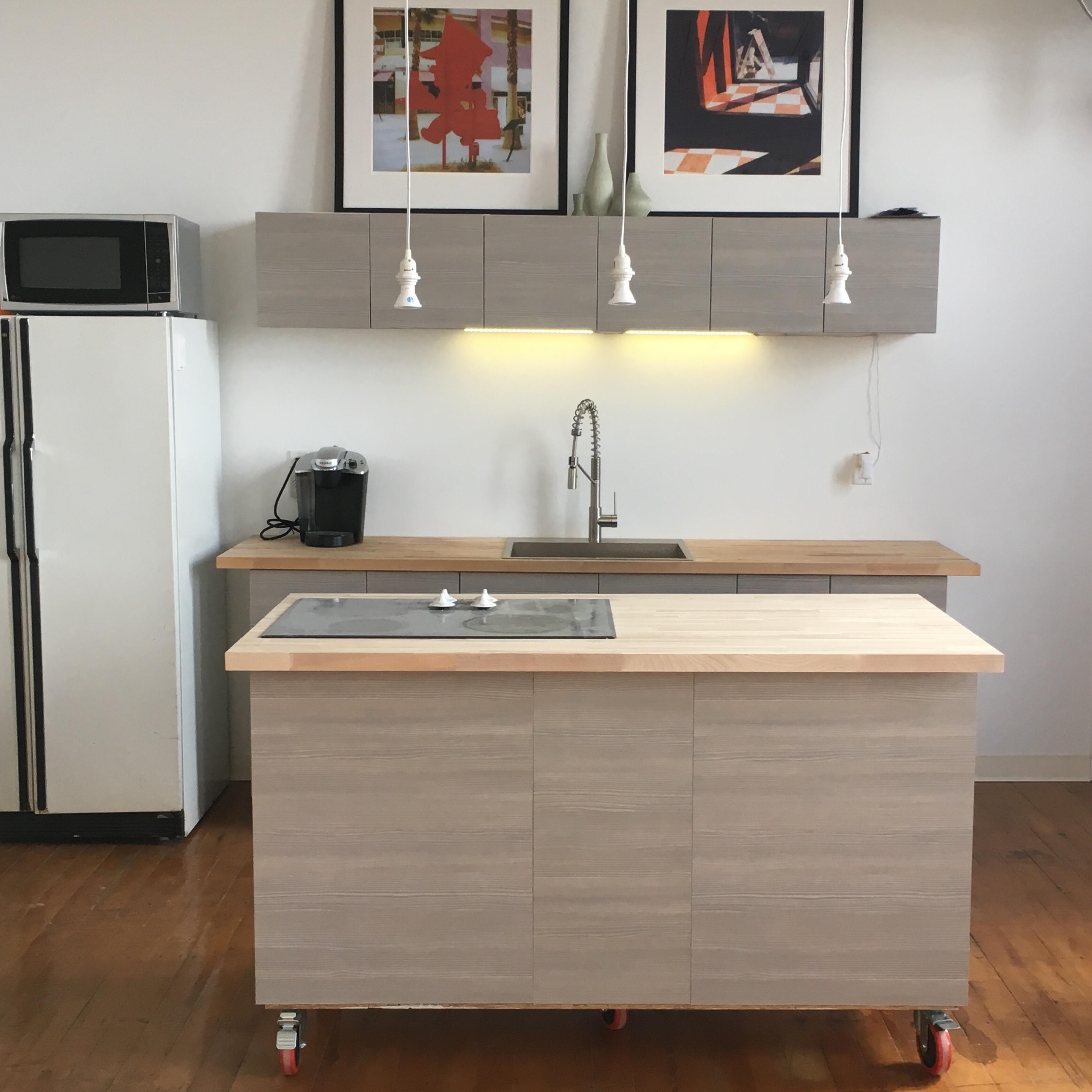 A modern kitchen with a mobile island, wall-mounted cabinets, and a stainless steel sink under pendant lights.