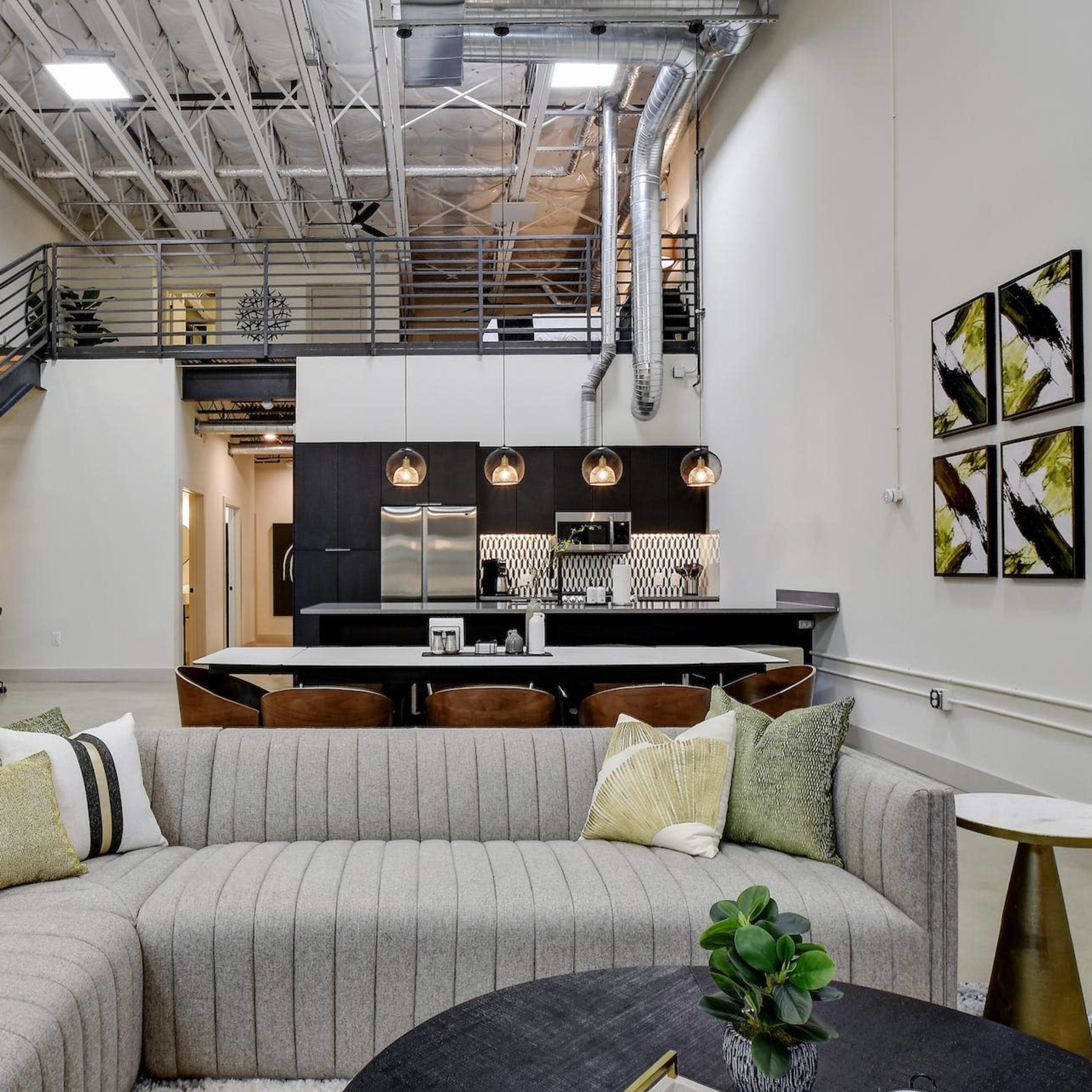 A contemporary open-concept living area with a large sectional sofa, a kitchen in the background, and a staircase leading to an upper level.