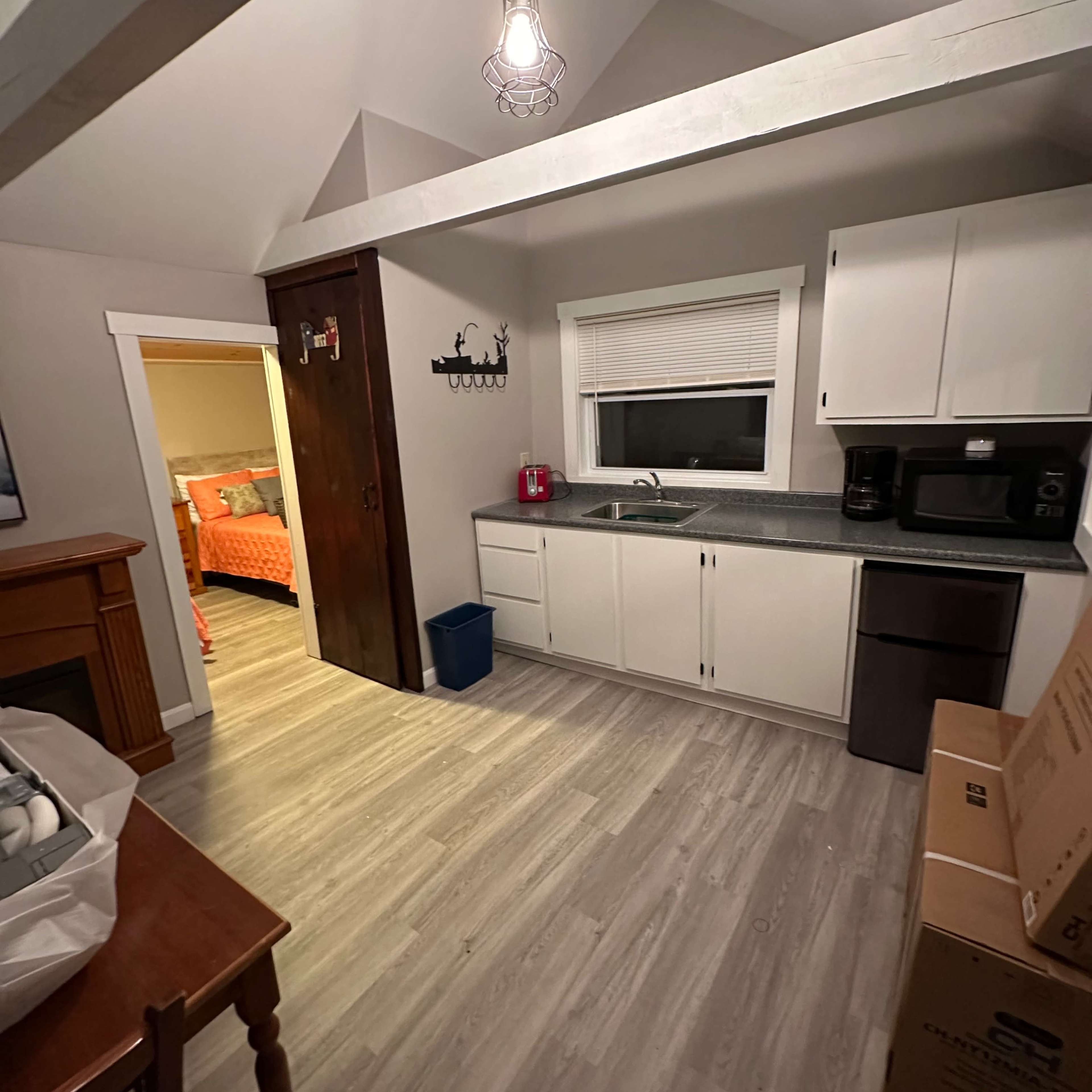 A small, well-lit kitchen area with white cabinets, a sink, and a doorway leading to an adjacent room.