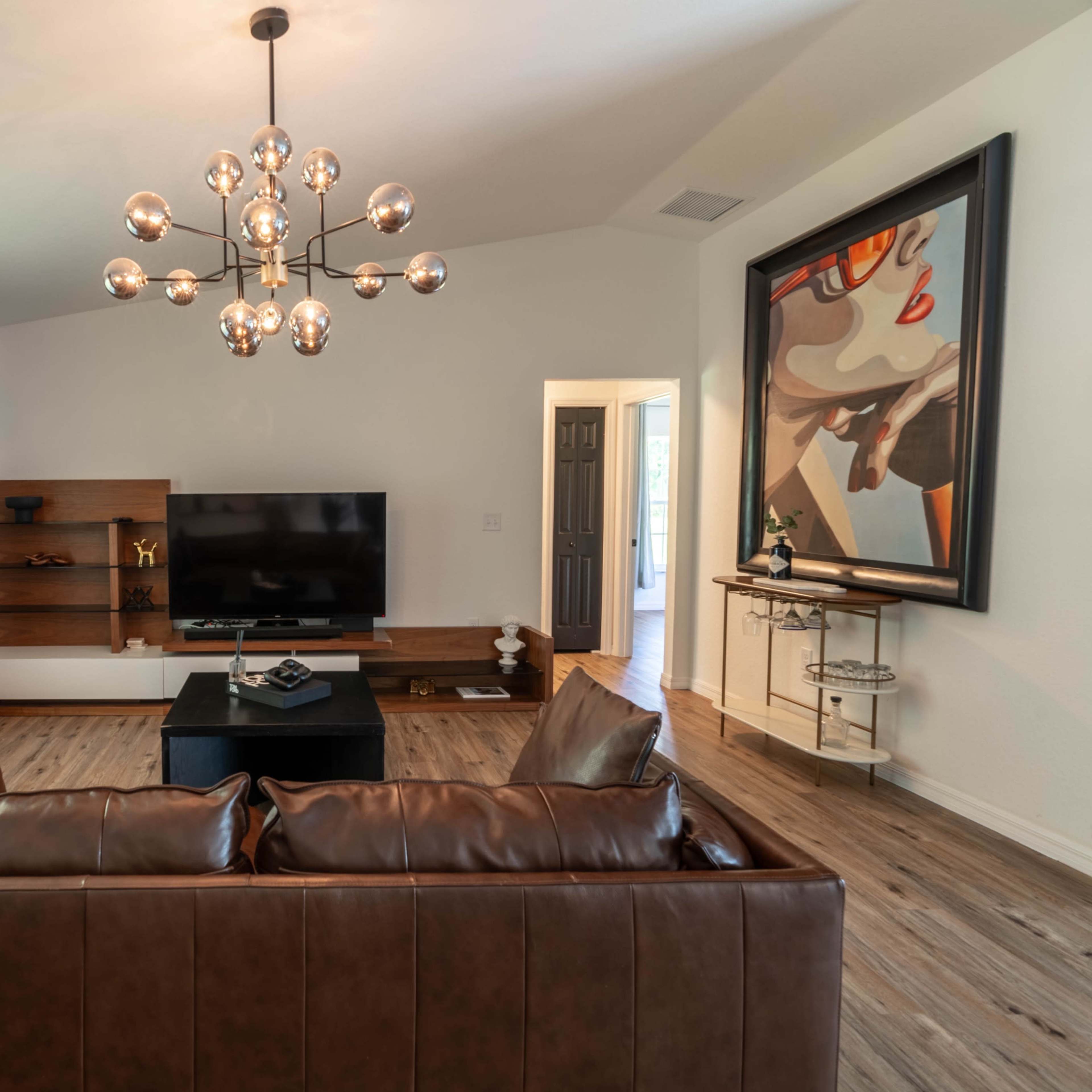 A modern living room features a leather sofa, a wall-mounted TV, and an artistic painting above a console table.