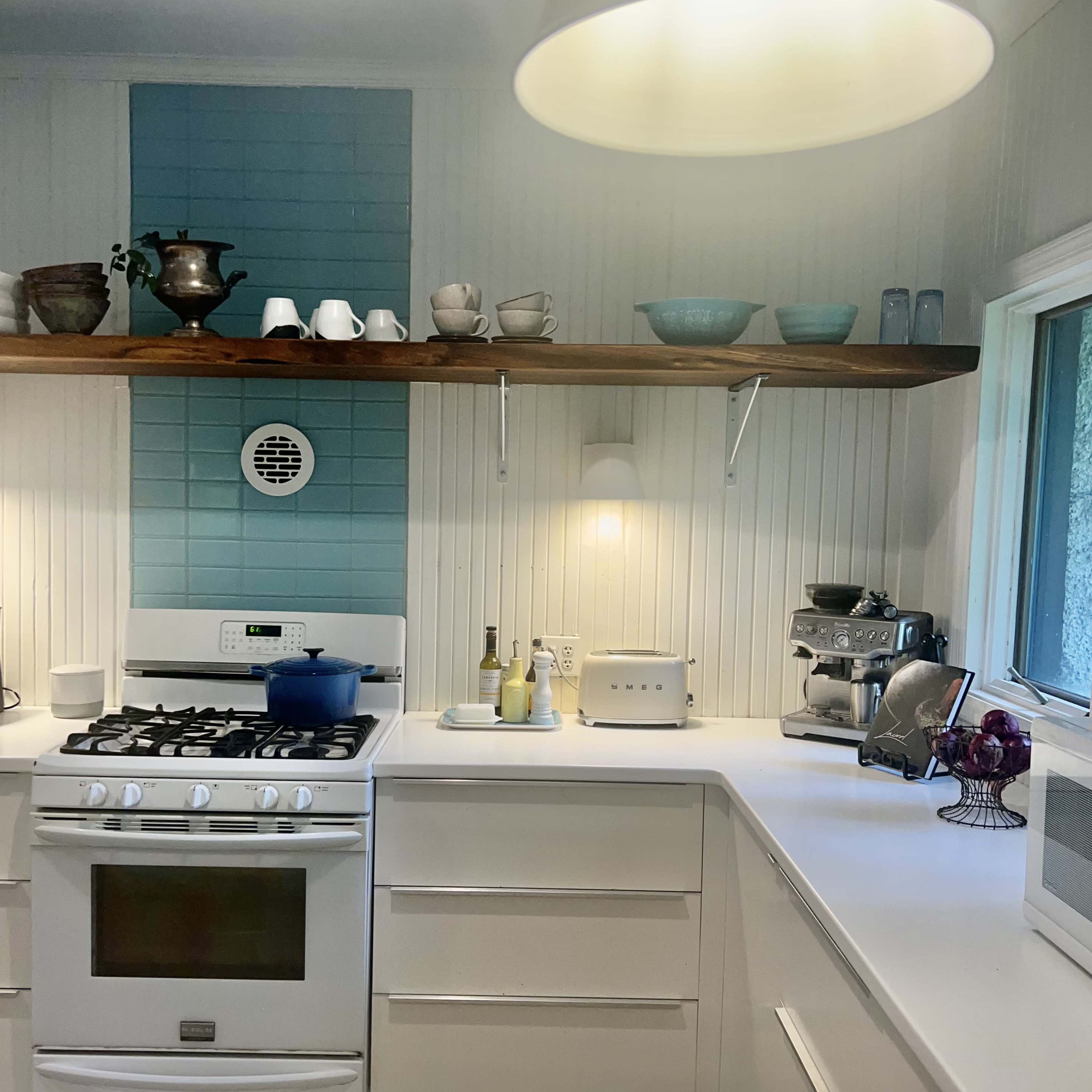 A modern kitchen with white cabinetry, a gas stove, and blue tile backsplash, featuring various kitchenware arranged on shelves above the counter.