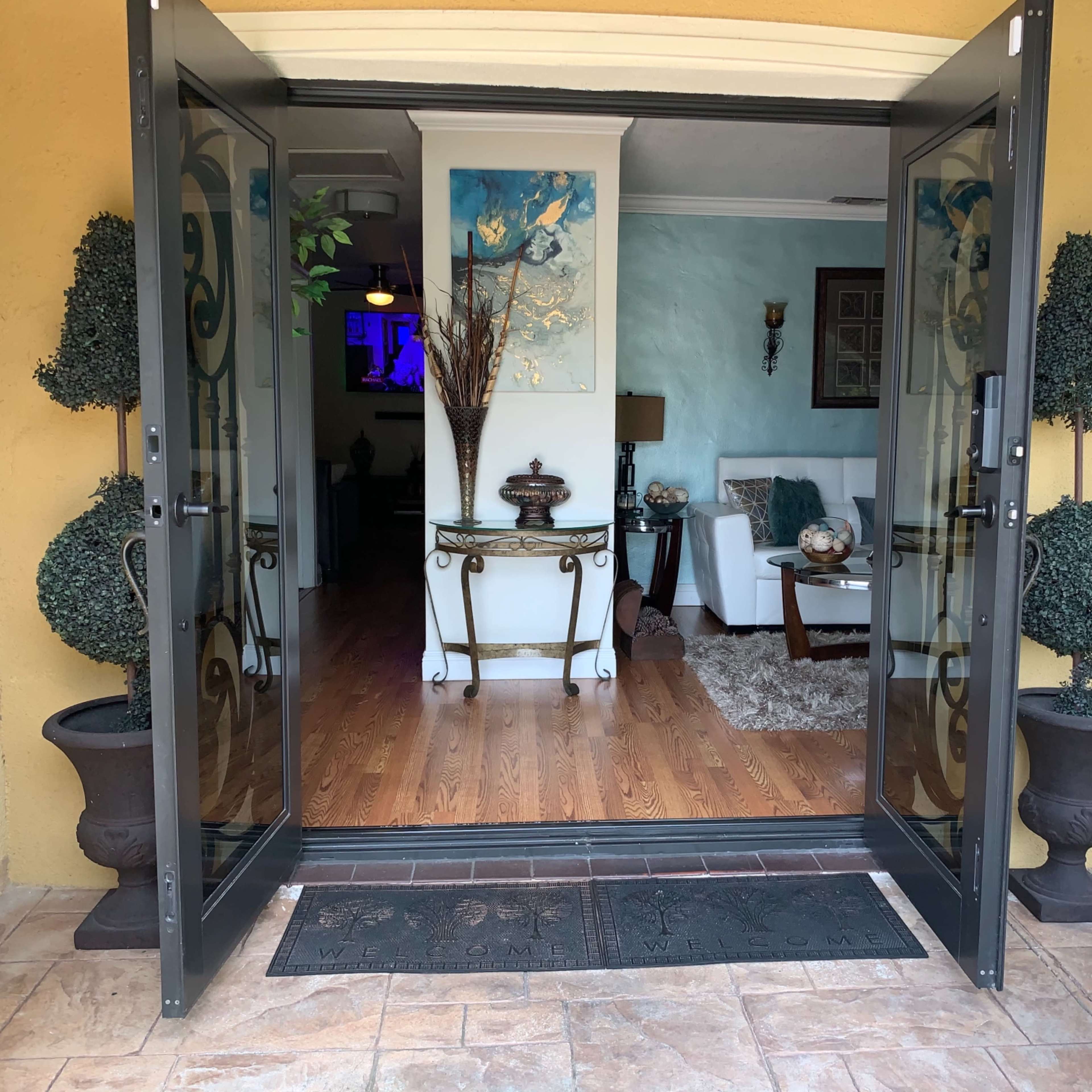 A pair of open glass doors leading into a well-decorated living room with wooden flooring and light-colored walls.