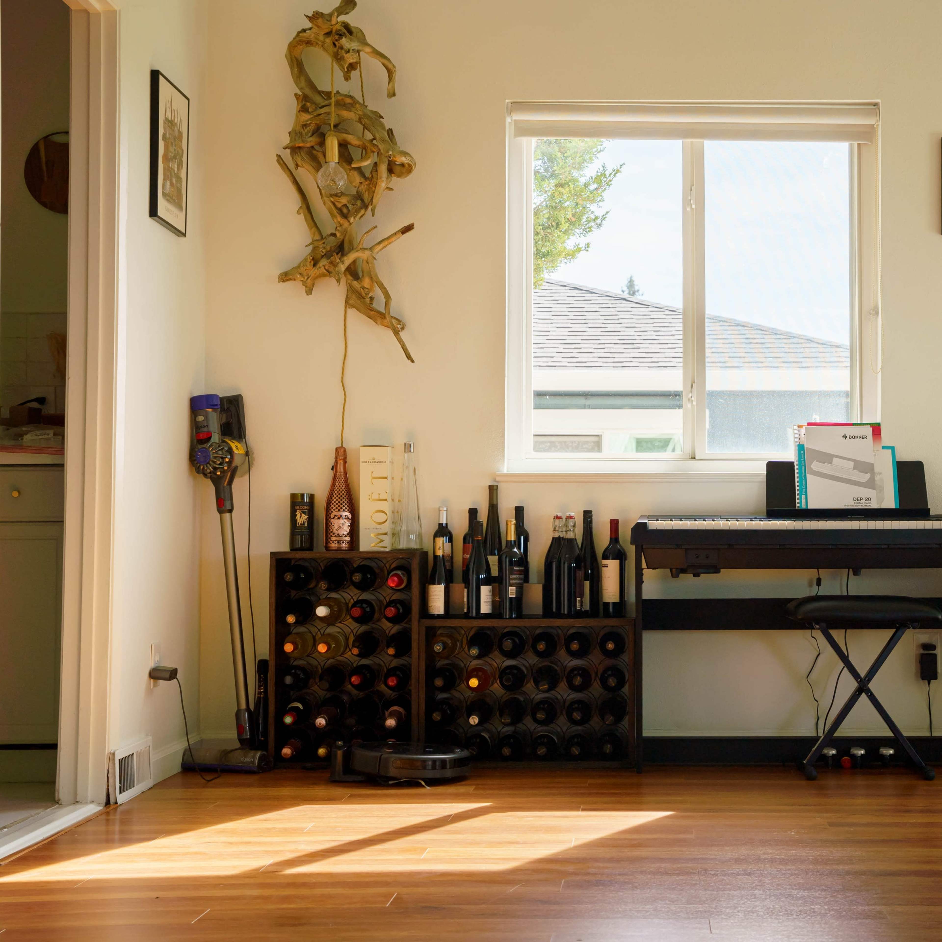 A room with a window, a wine rack filled with bottles, and a digital piano positioned against a wall.