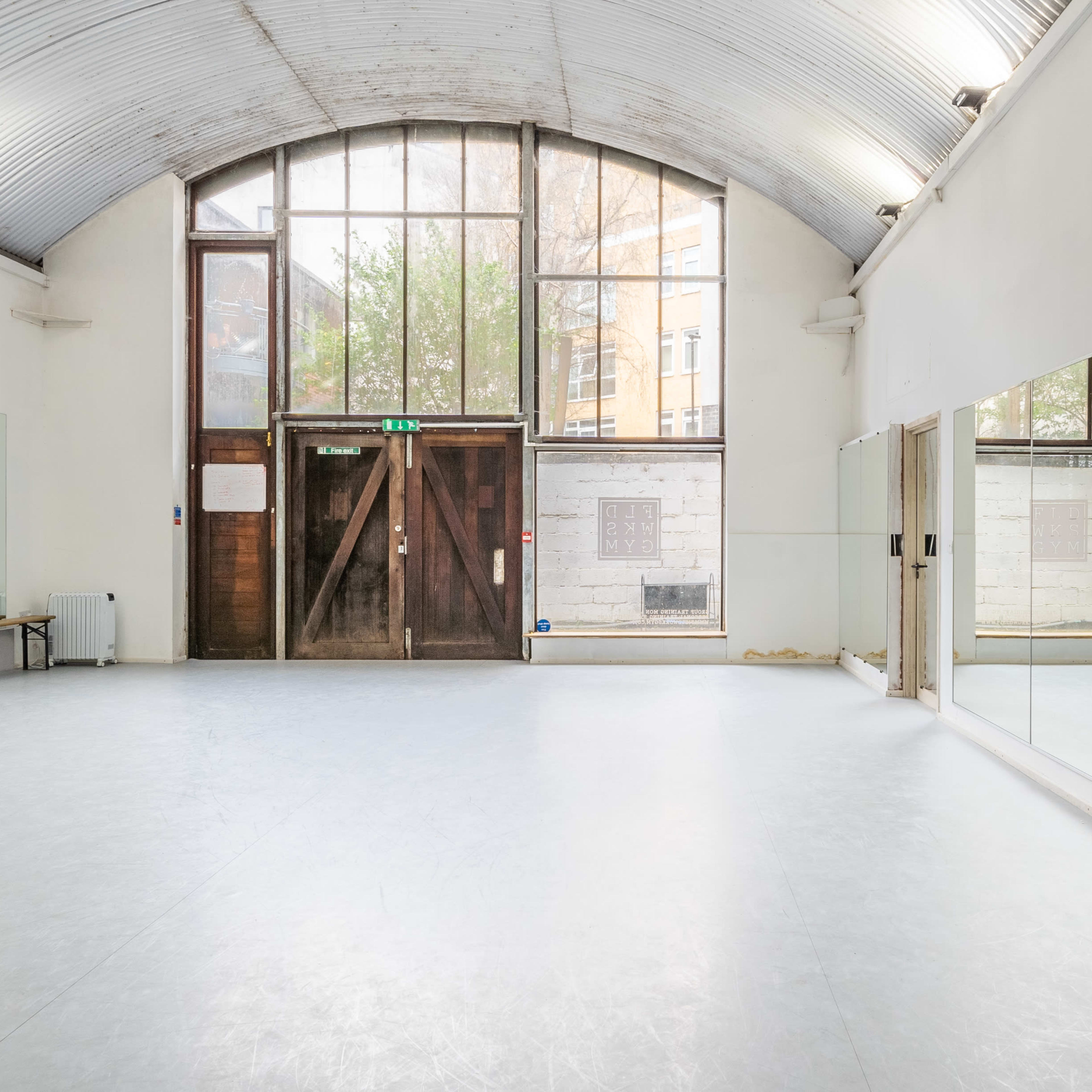 A spacious dance studio featuring large mirrors along one wall and tall windows allowing natural light to enter.