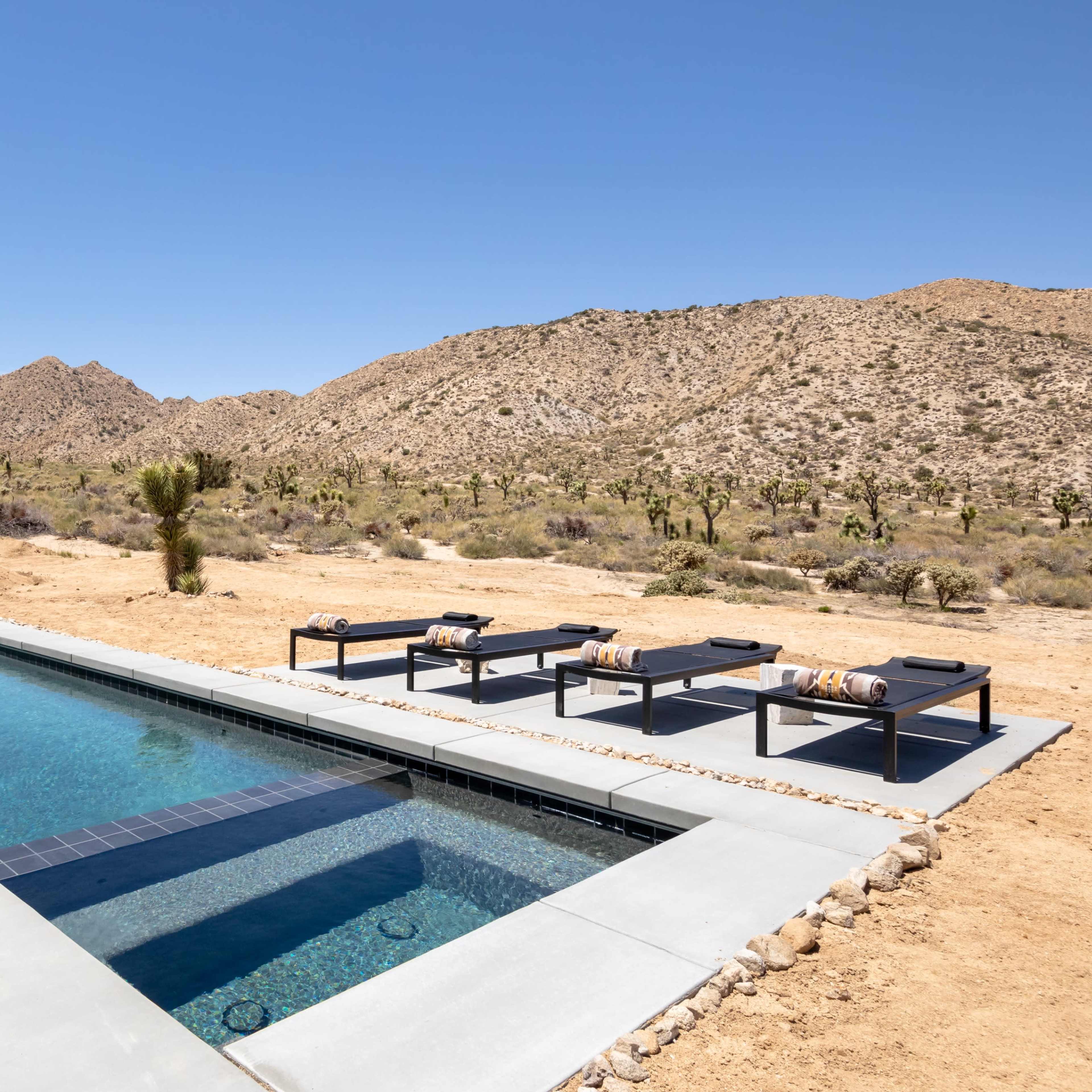 A swimming pool with adjacent loungers is set against a backdrop of rocky hills and desert vegetation.
