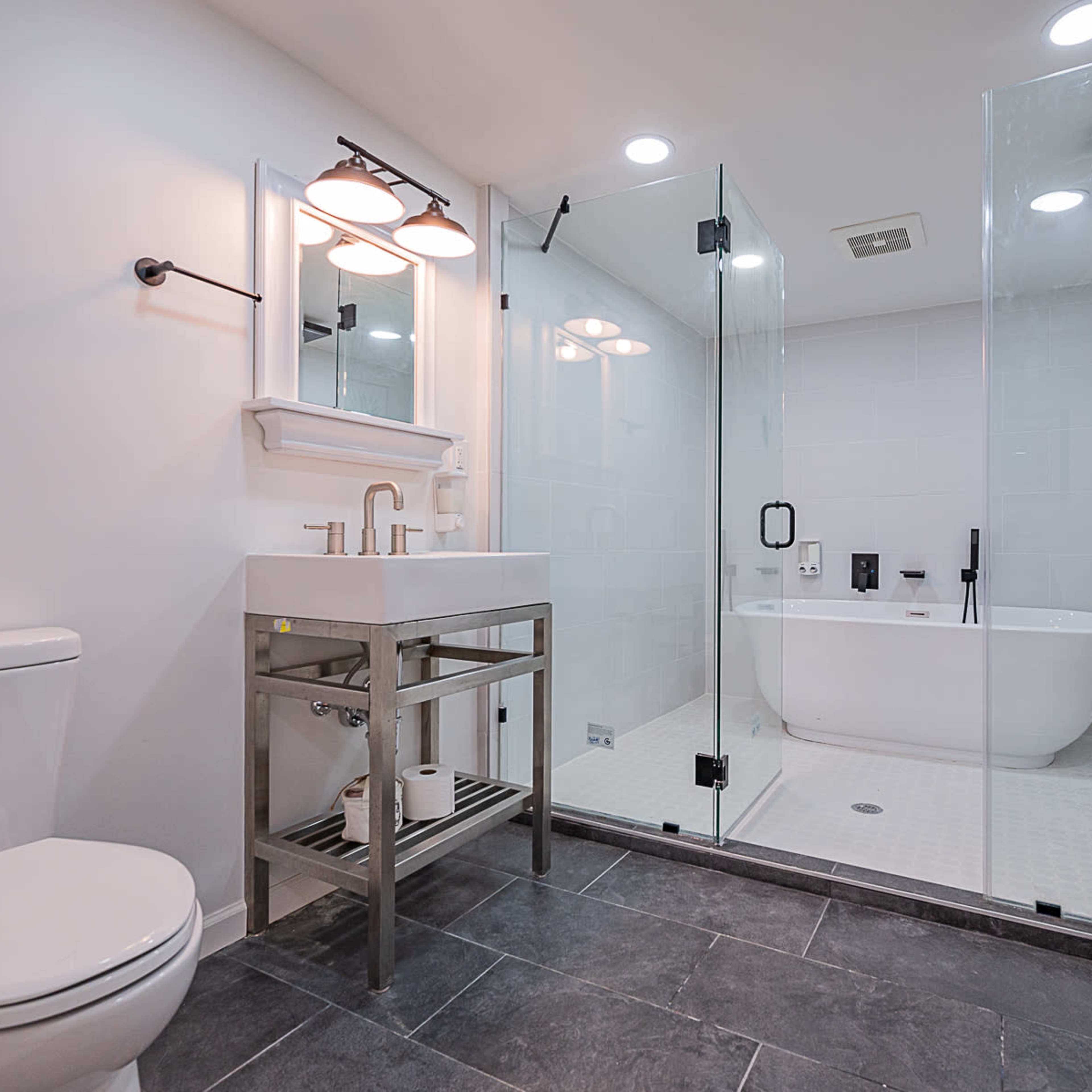 A modern bathroom featuring a glass-enclosed shower, a freestanding bathtub, a wall-mounted mirror, and a sleek sink with a storage shelf.