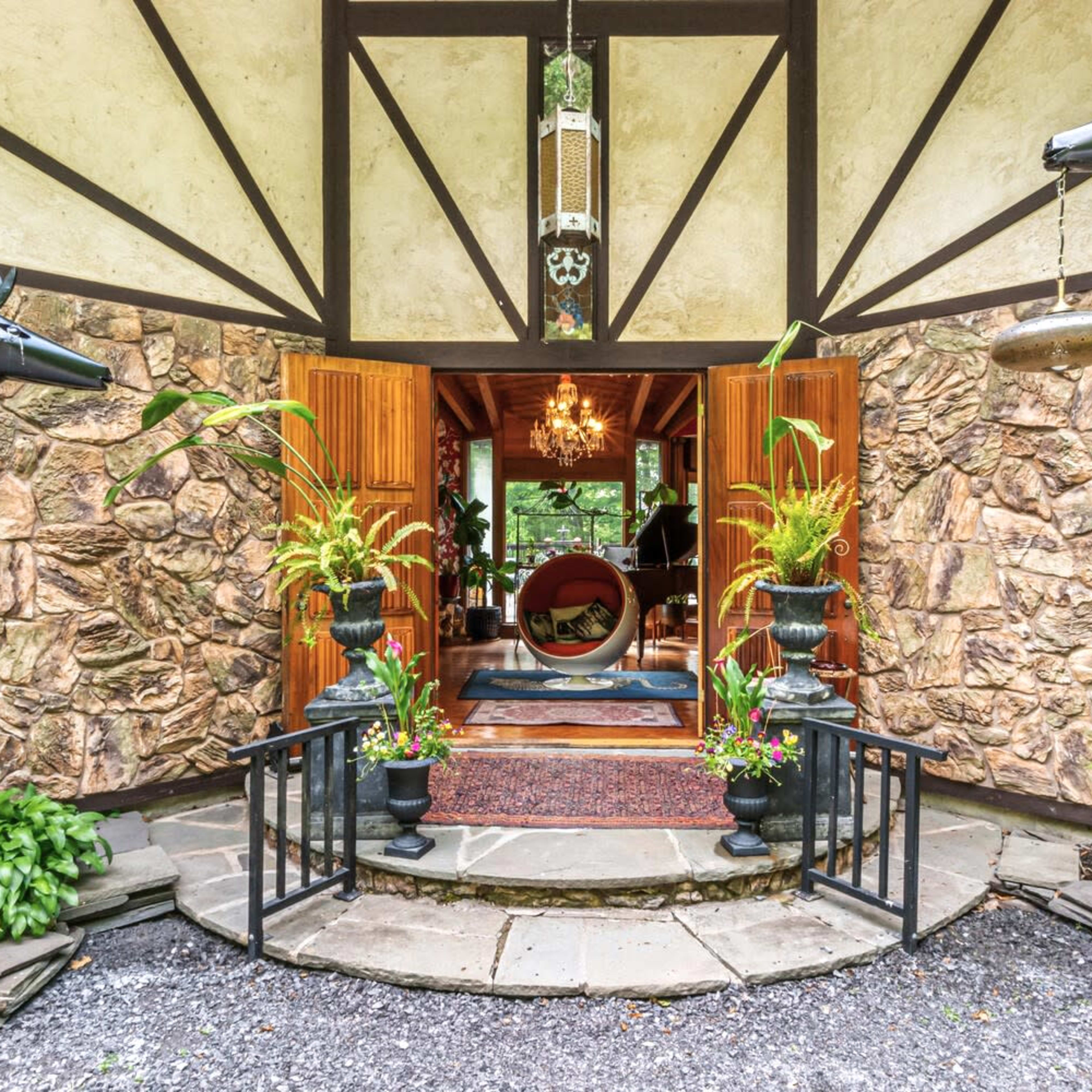 The entrance of a stone house is flanked by two black horse sculptures, leading to a welcoming interior with a round seating area and decorative plants.