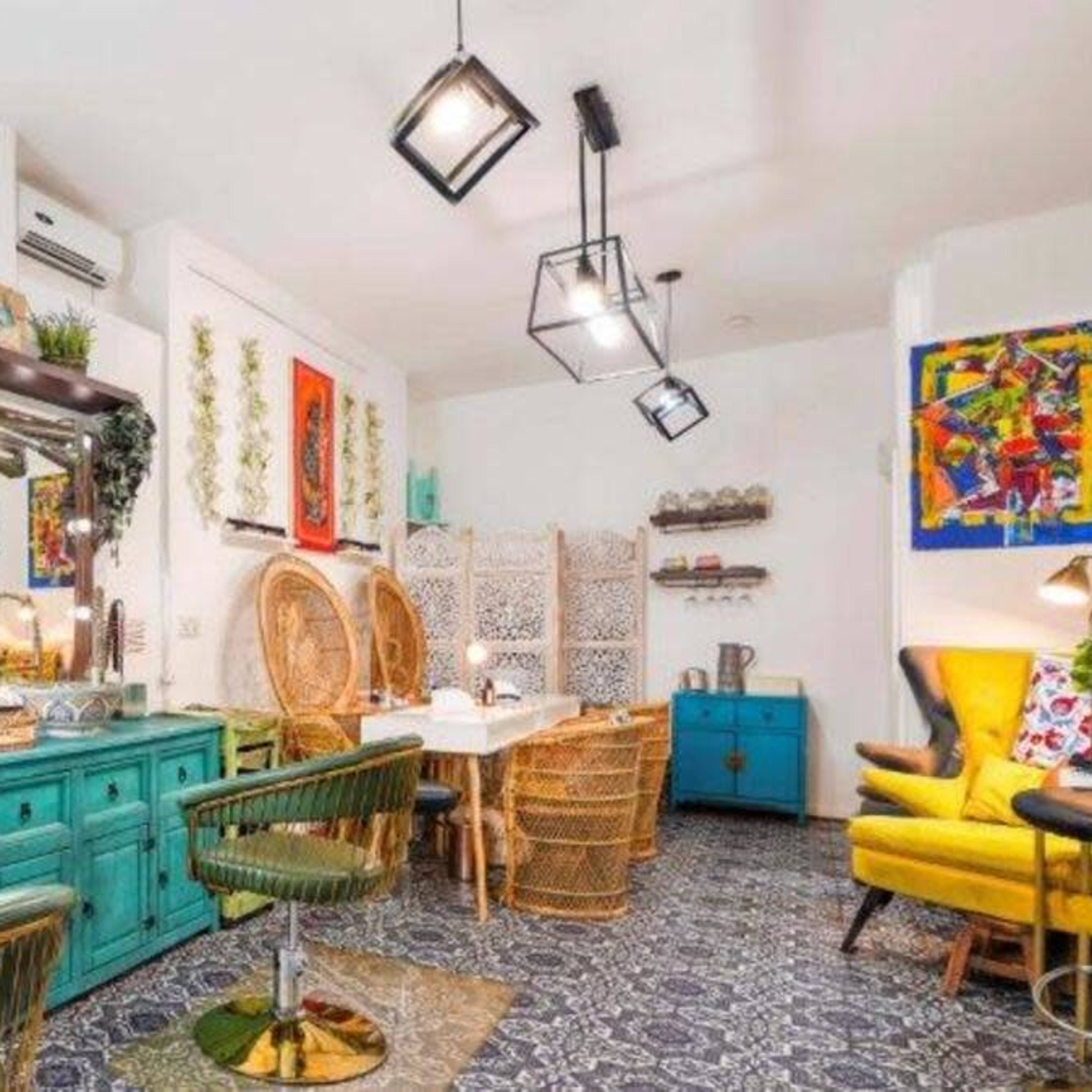 A brightly lit café with turquoise furniture, decorative mirrors, and plants, featuring a mix of rattan chairs and a dining table.