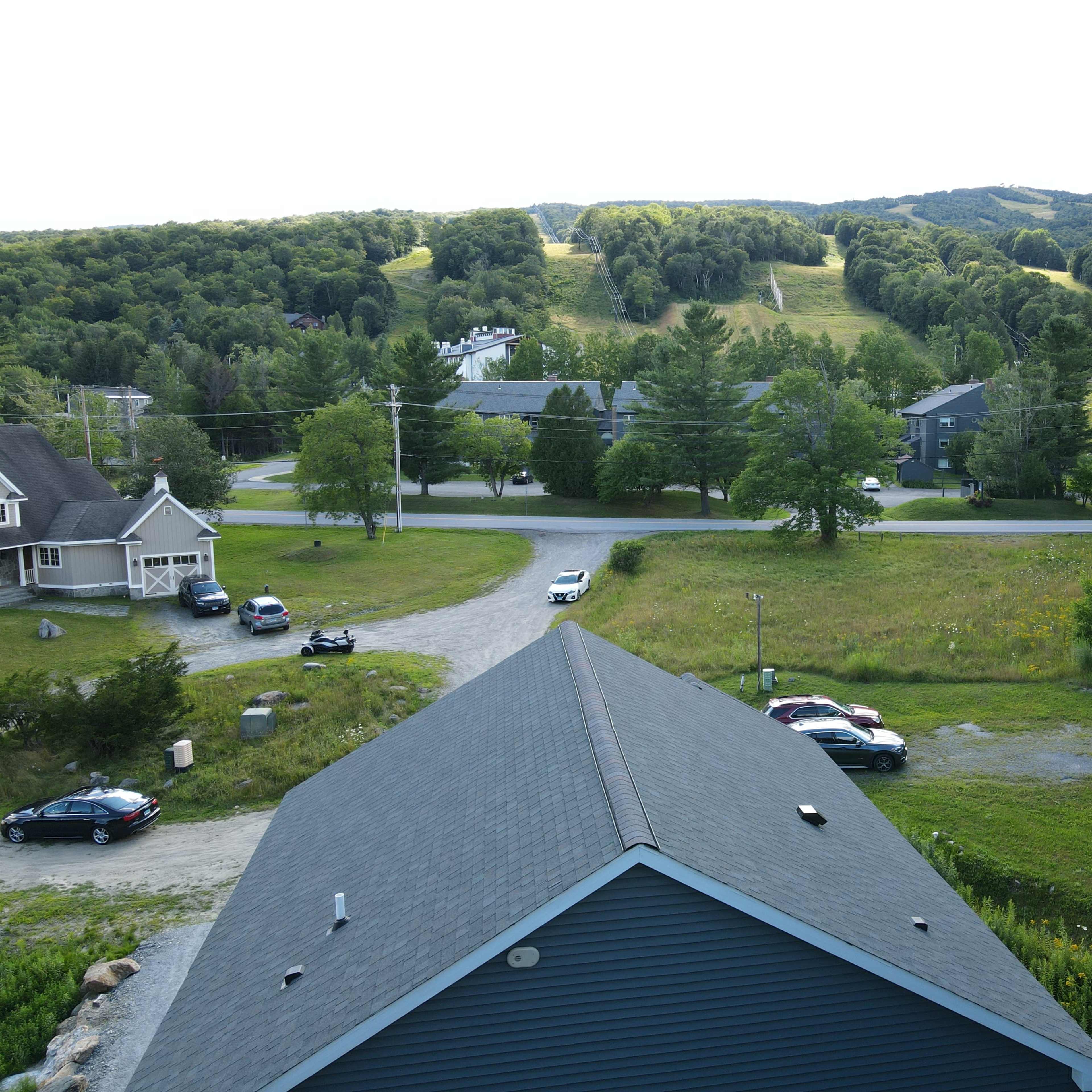 A residential area with several houses, a gravel road, and a view of a green hillside in the background.