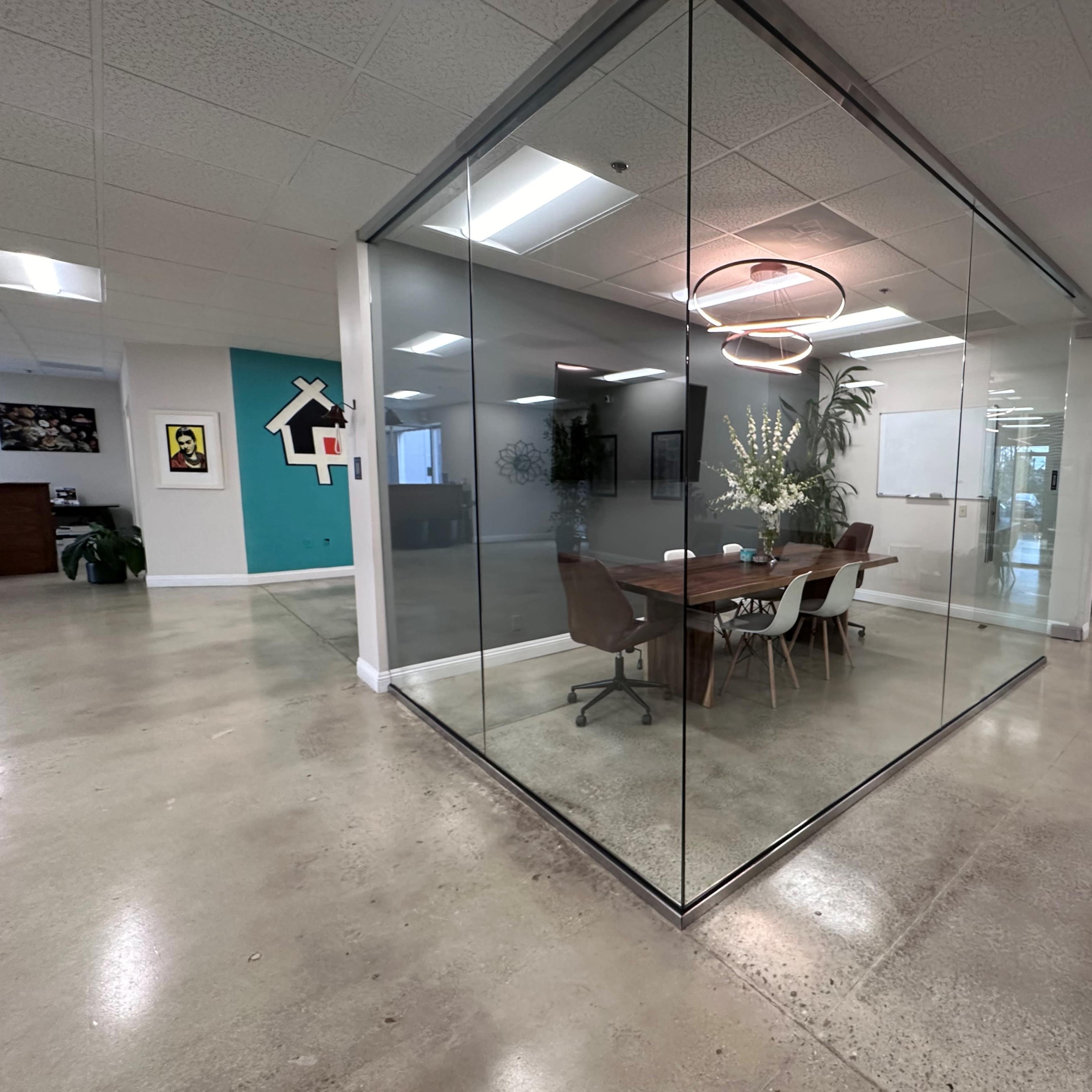 A modern office space featuring a glass-walled meeting room with a wooden table and chairs, surrounded by a minimalist decor.