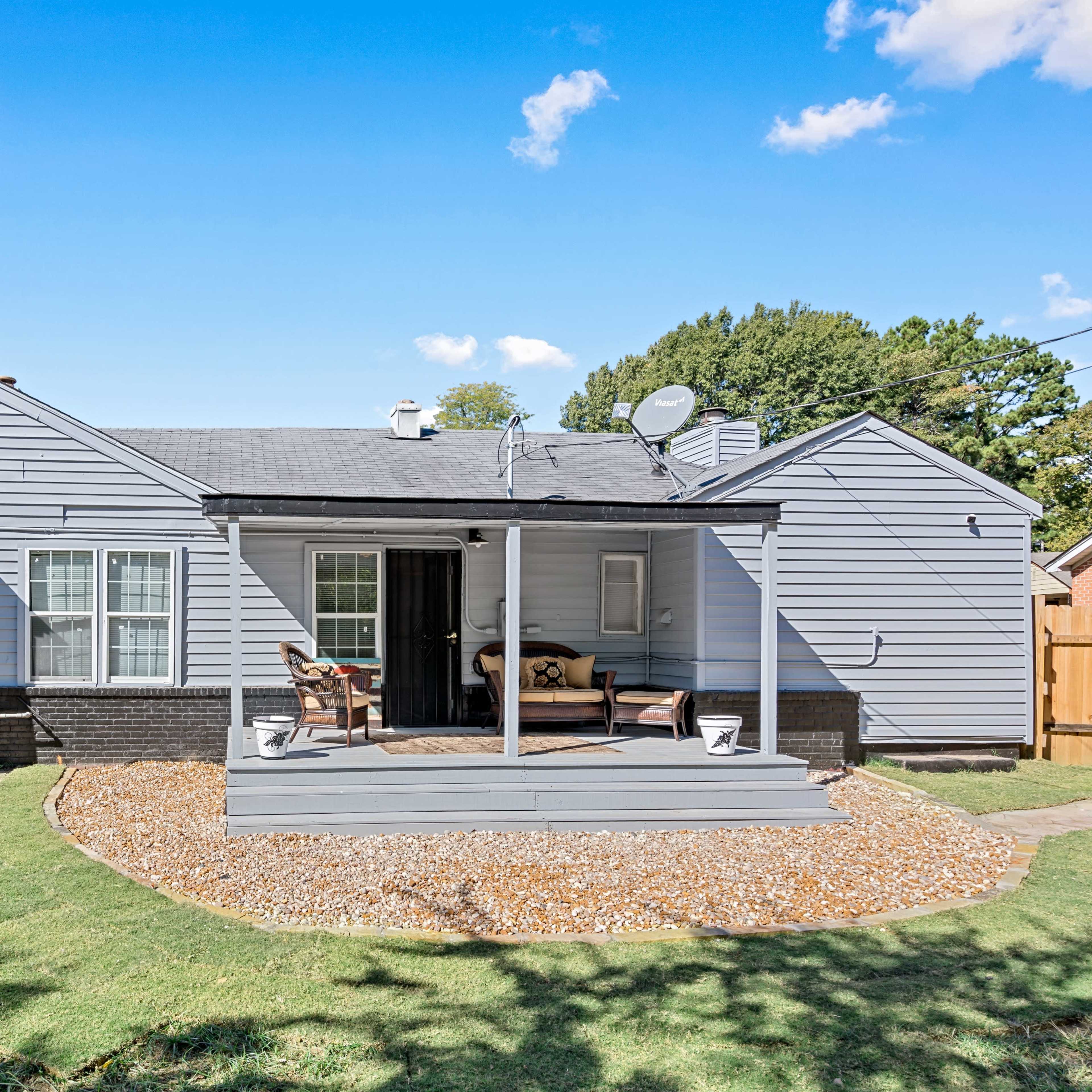 A single-story gray house with a front porch and a landscaped yard featuring a gravel circle.