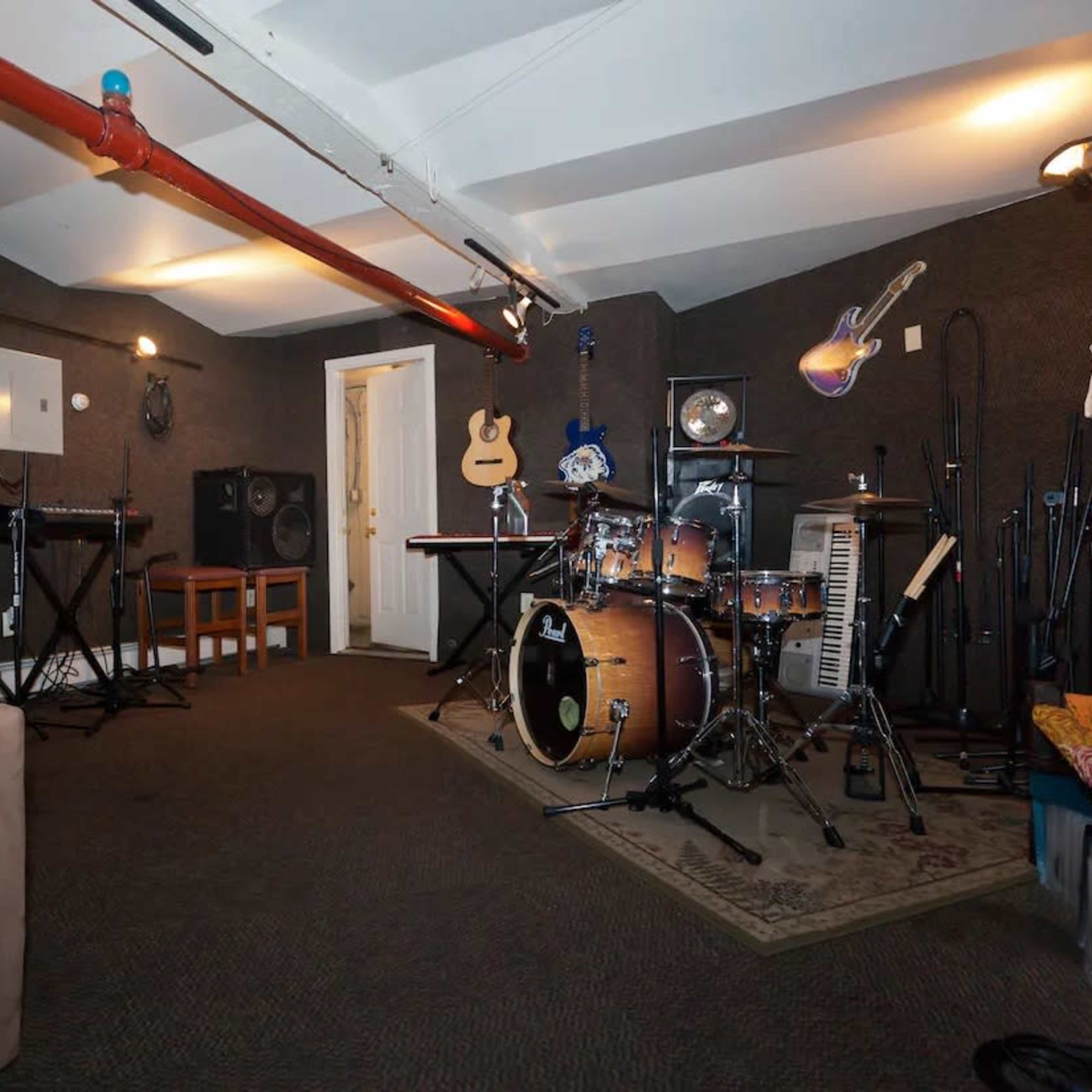 A soundproof music studio featuring a drum set, several guitars, keyboards, microphones, and audio equipment arranged around the room.