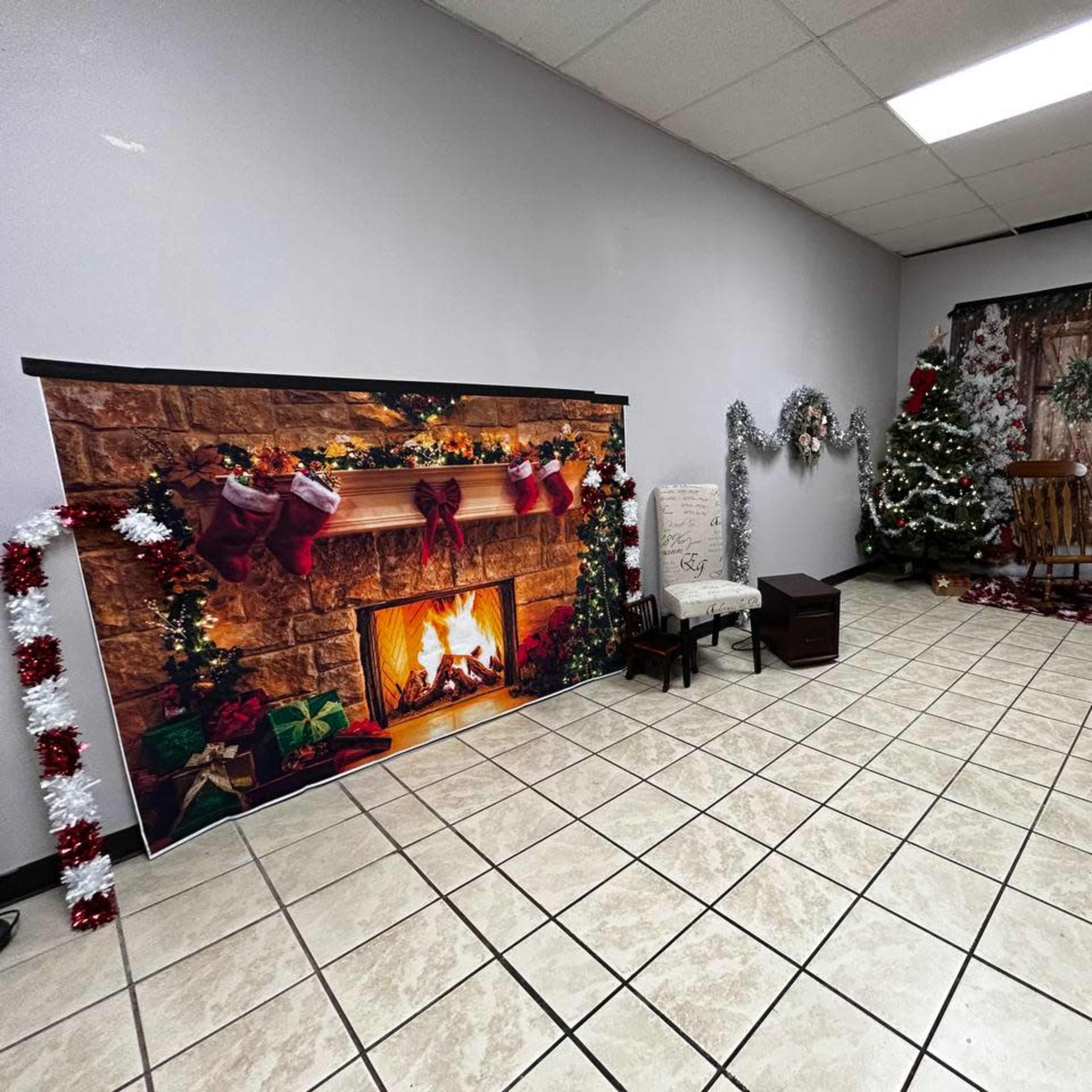 A decorated room featuring a faux fireplace with stockings, a Christmas tree, and festive props arranged along the walls.