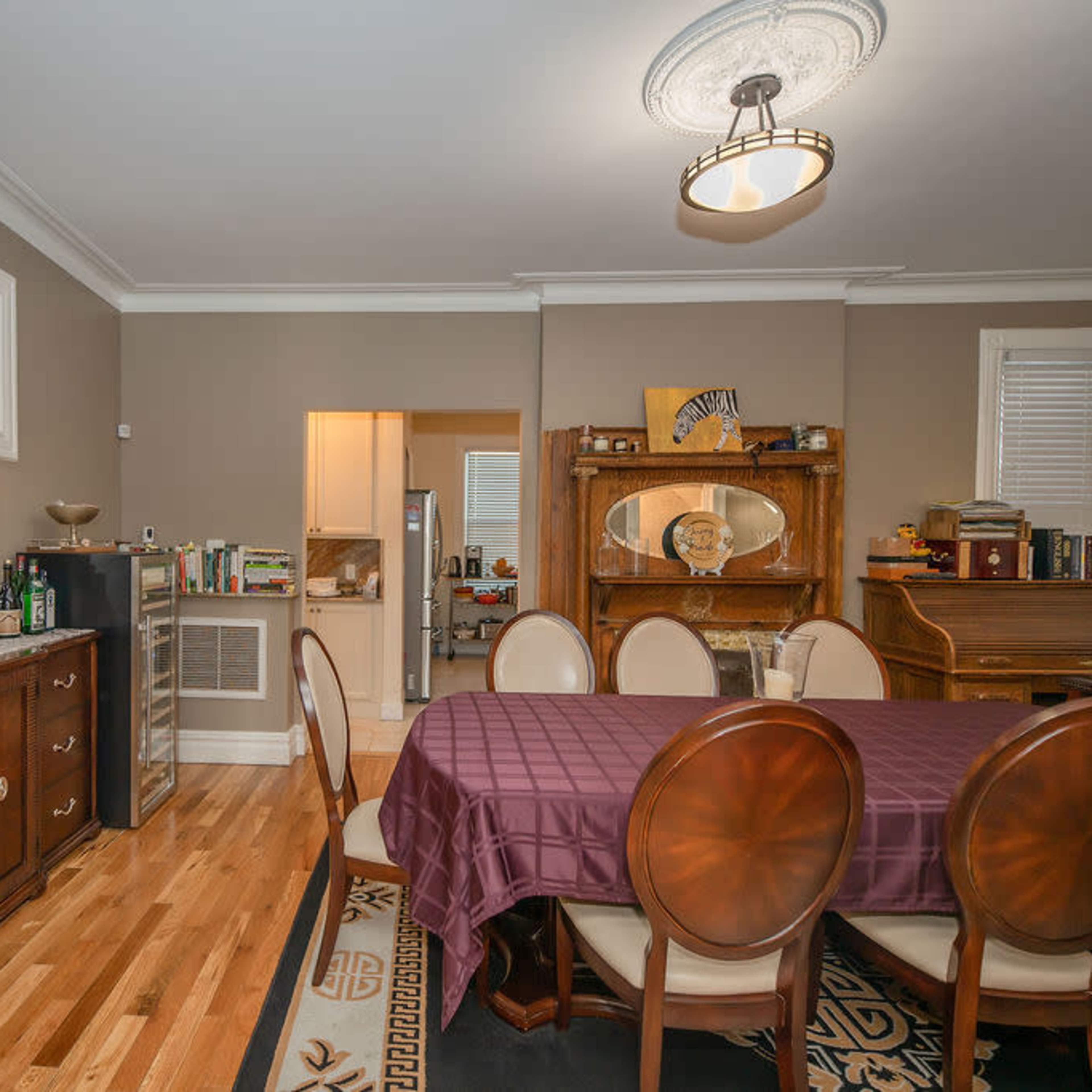 The dining room features a wooden table surrounded by chairs, with a sideboard, a piano in the corner, and a stained glass window above.