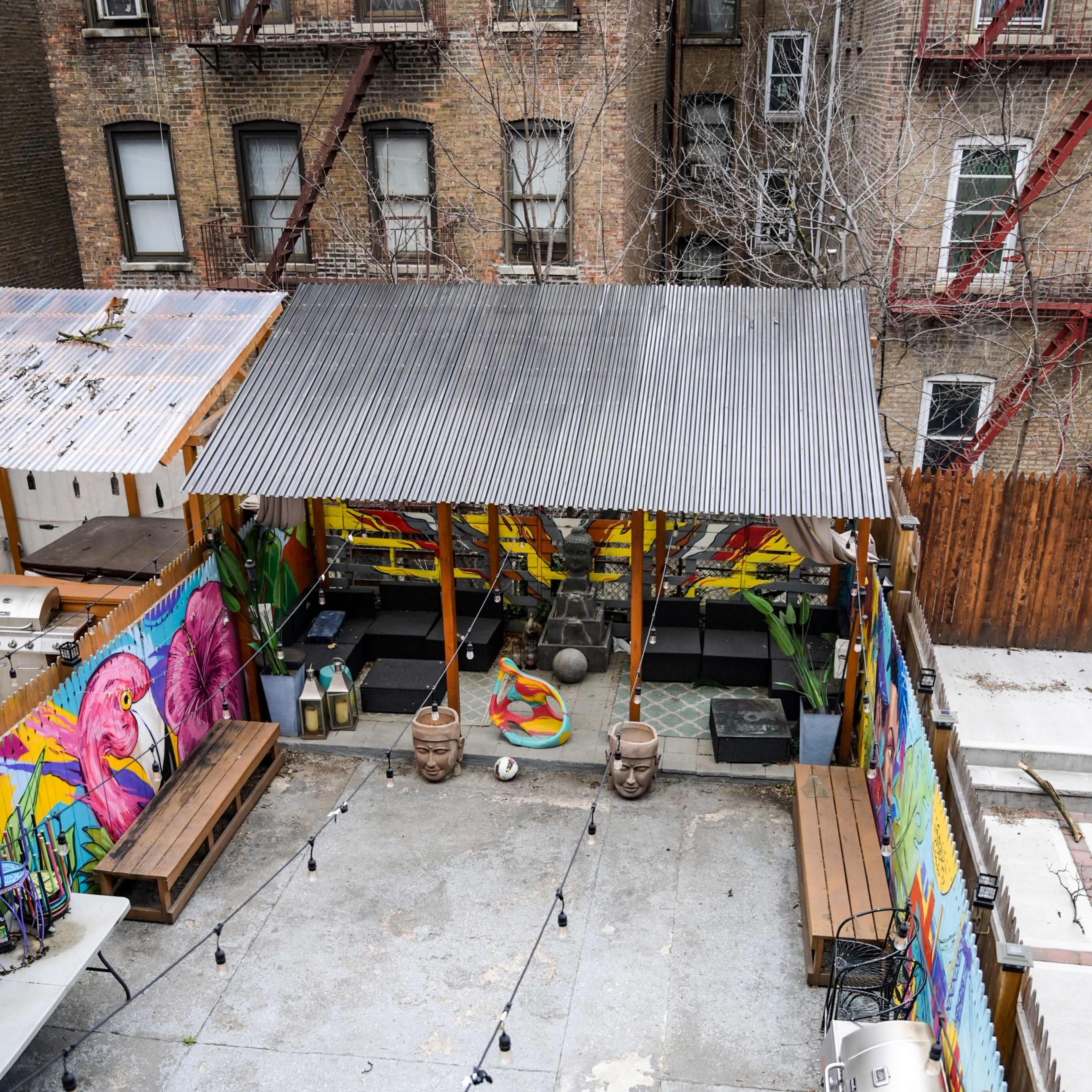 A colorful outdoor patio area with benches, a grill, string lights, and vibrant murals on the walls.