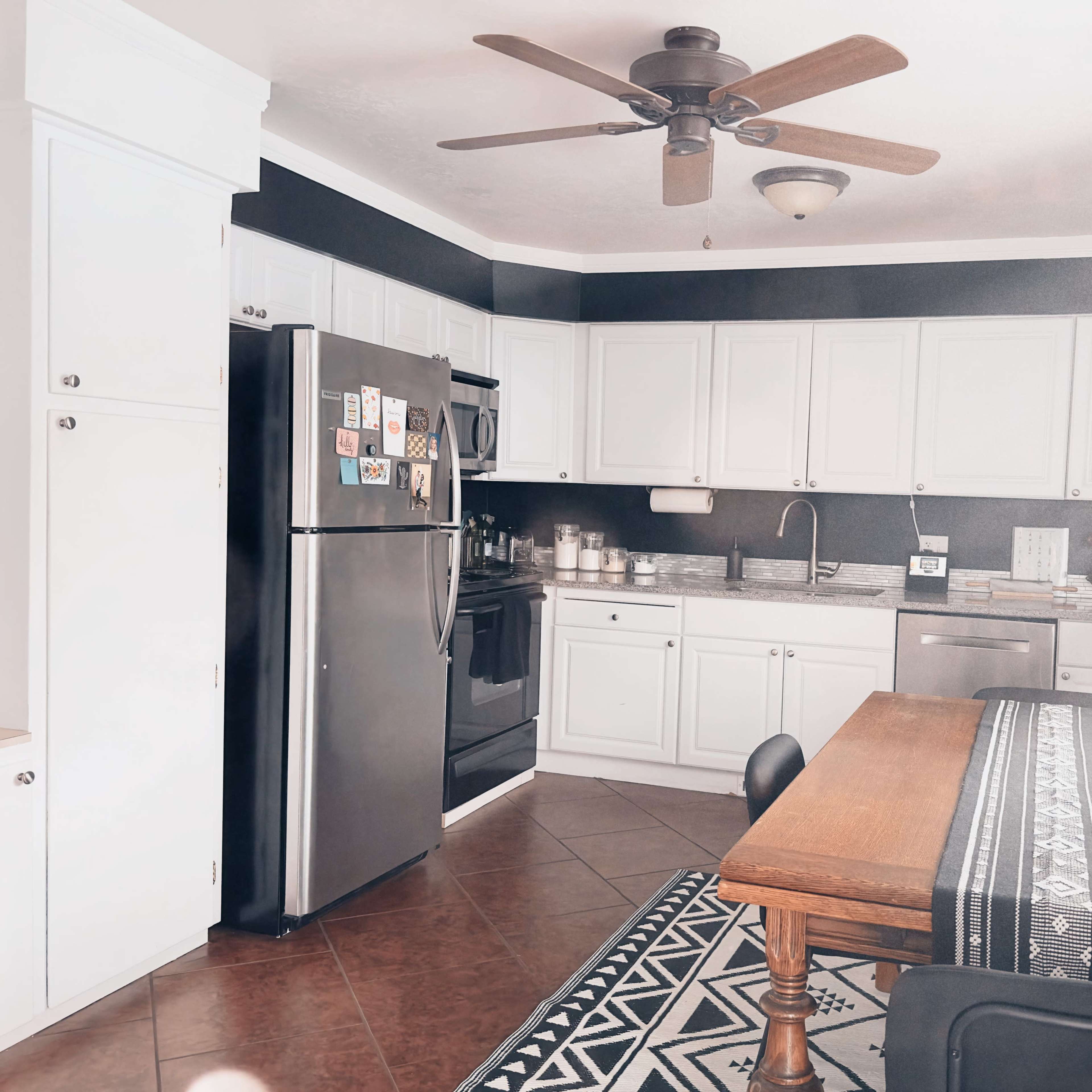 A kitchen with white cabinets, a black refrigerator, stainless steel appliances, and a wooden dining table with a patterned runner.