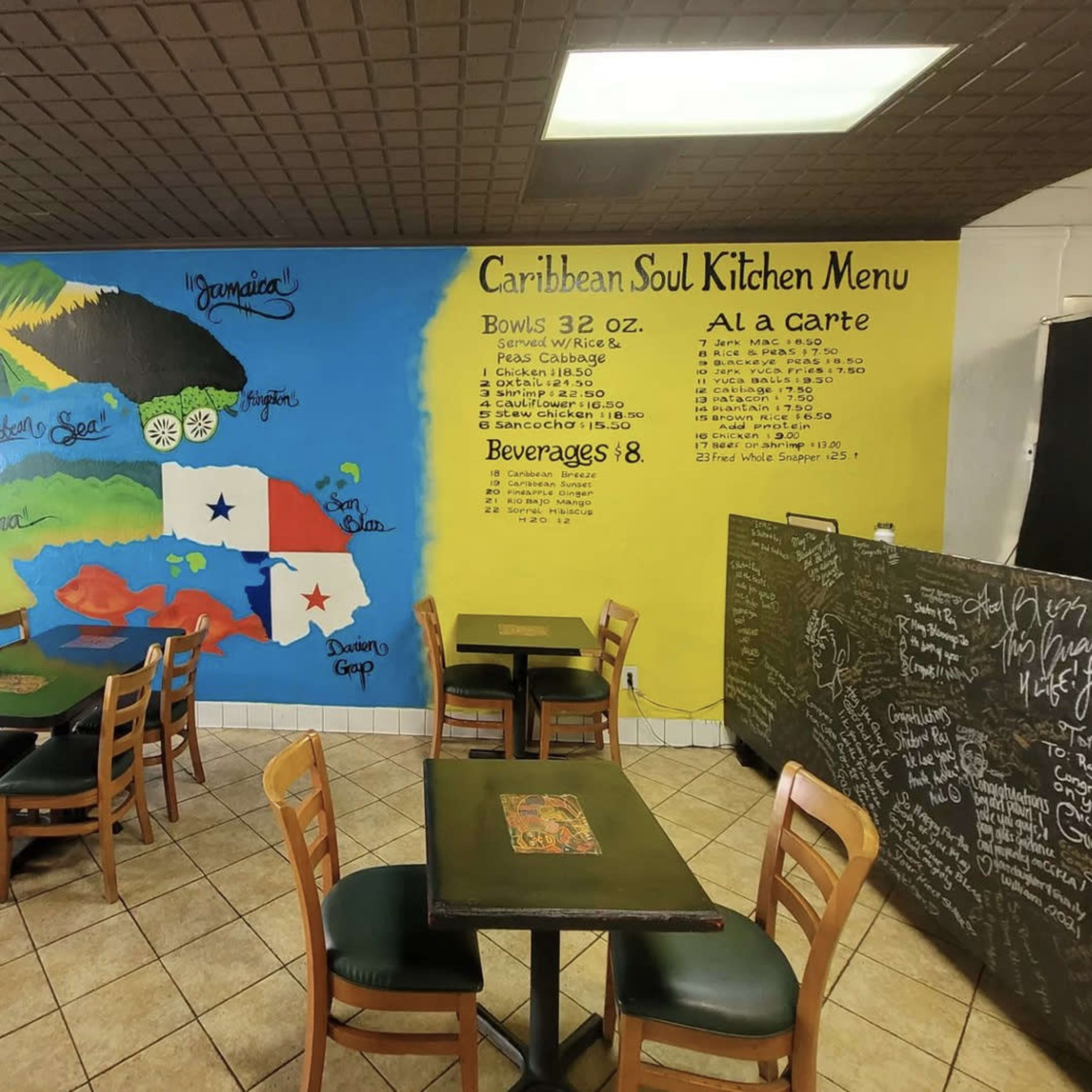 A Caribbean-themed restaurant interior with a colorful mural depicting the Caribbean islands on the wall and a menu list hand-painted in yellow.