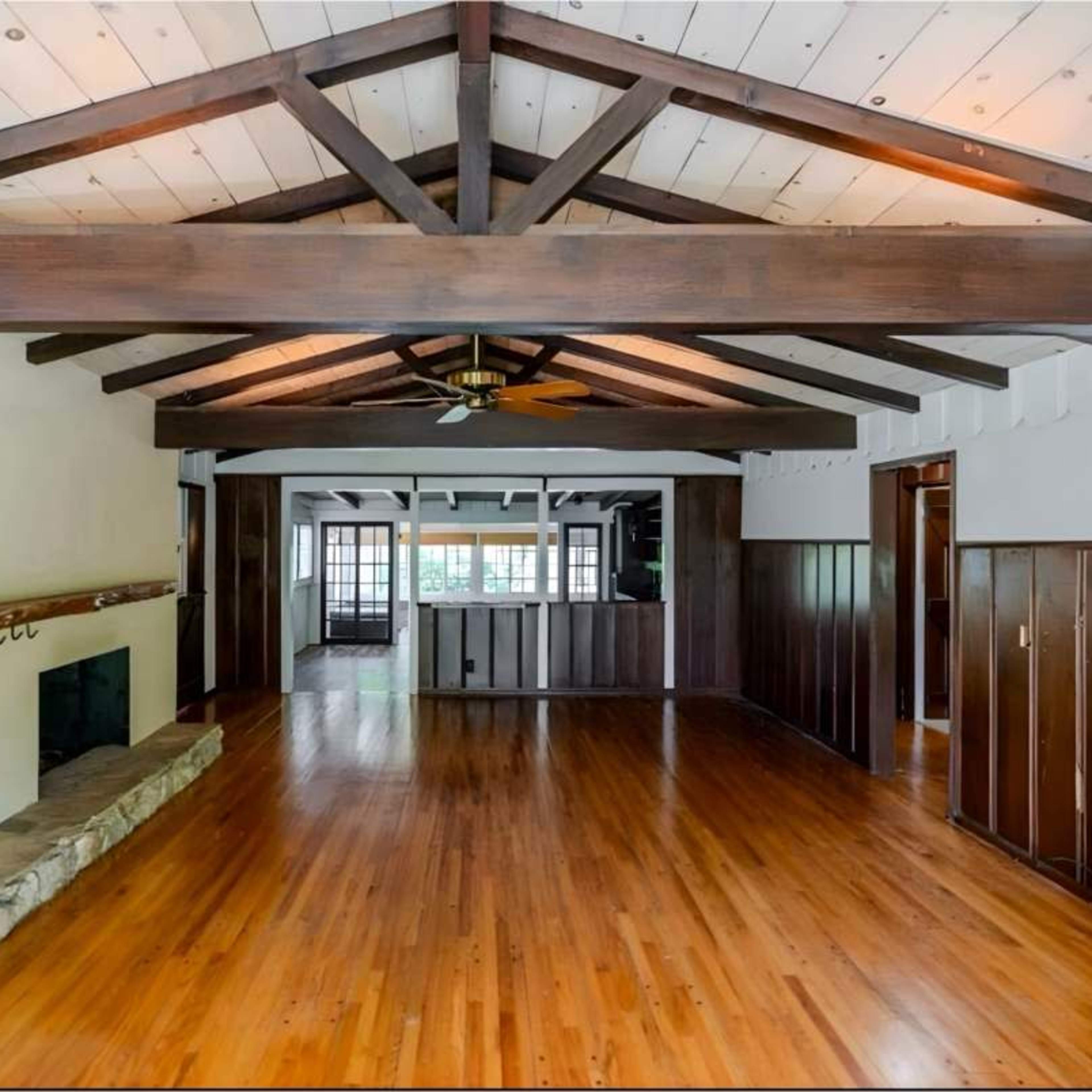 A spacious interior room featuring exposed wooden beams, a stone fireplace, and hardwood floors.