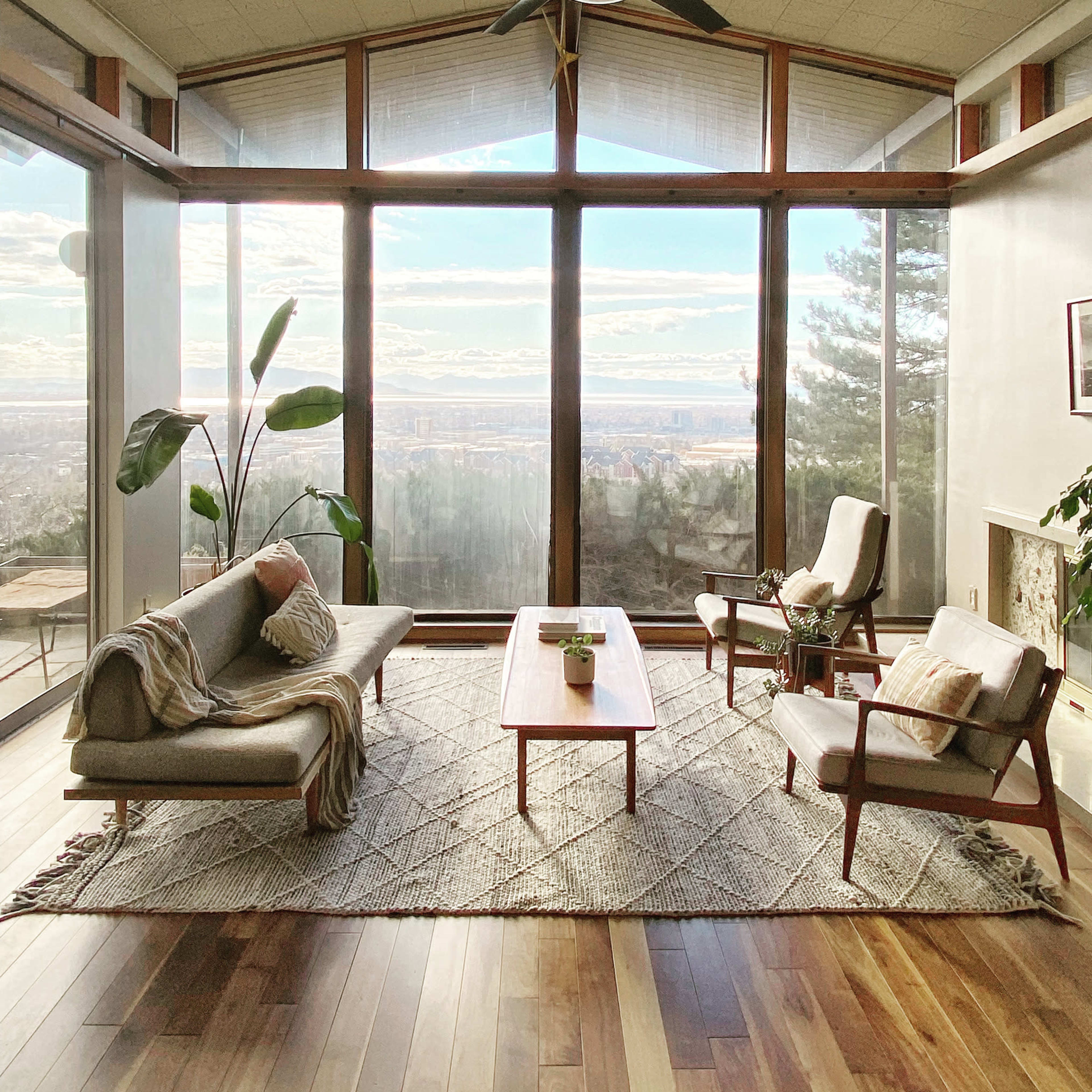 The living room features a large window with a view of the landscape, furnished with a sofa, two armchairs, a coffee table, and a plant.