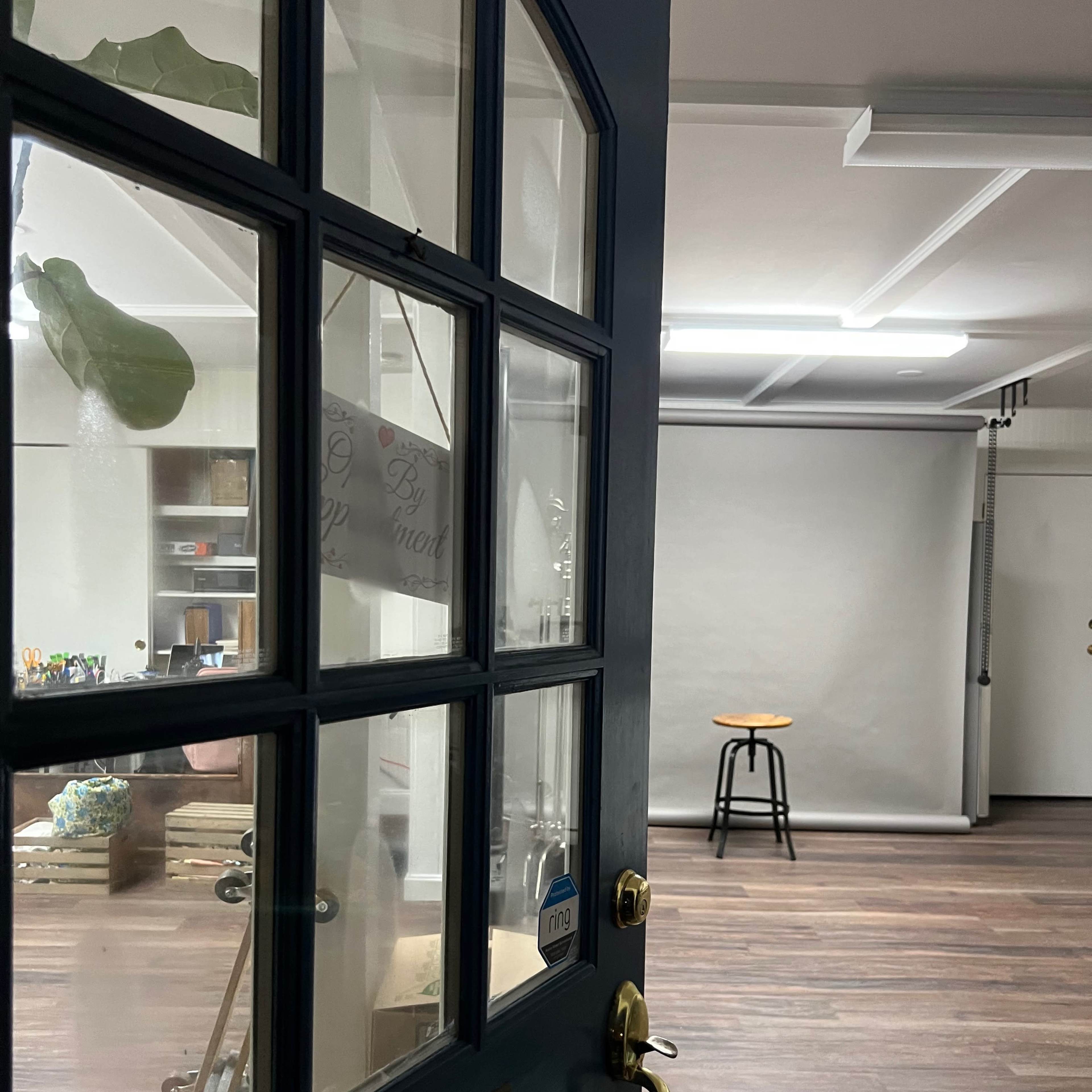 A partially open blue door leading into a sparsely furnished studio with a stool and a plain backdrop.
