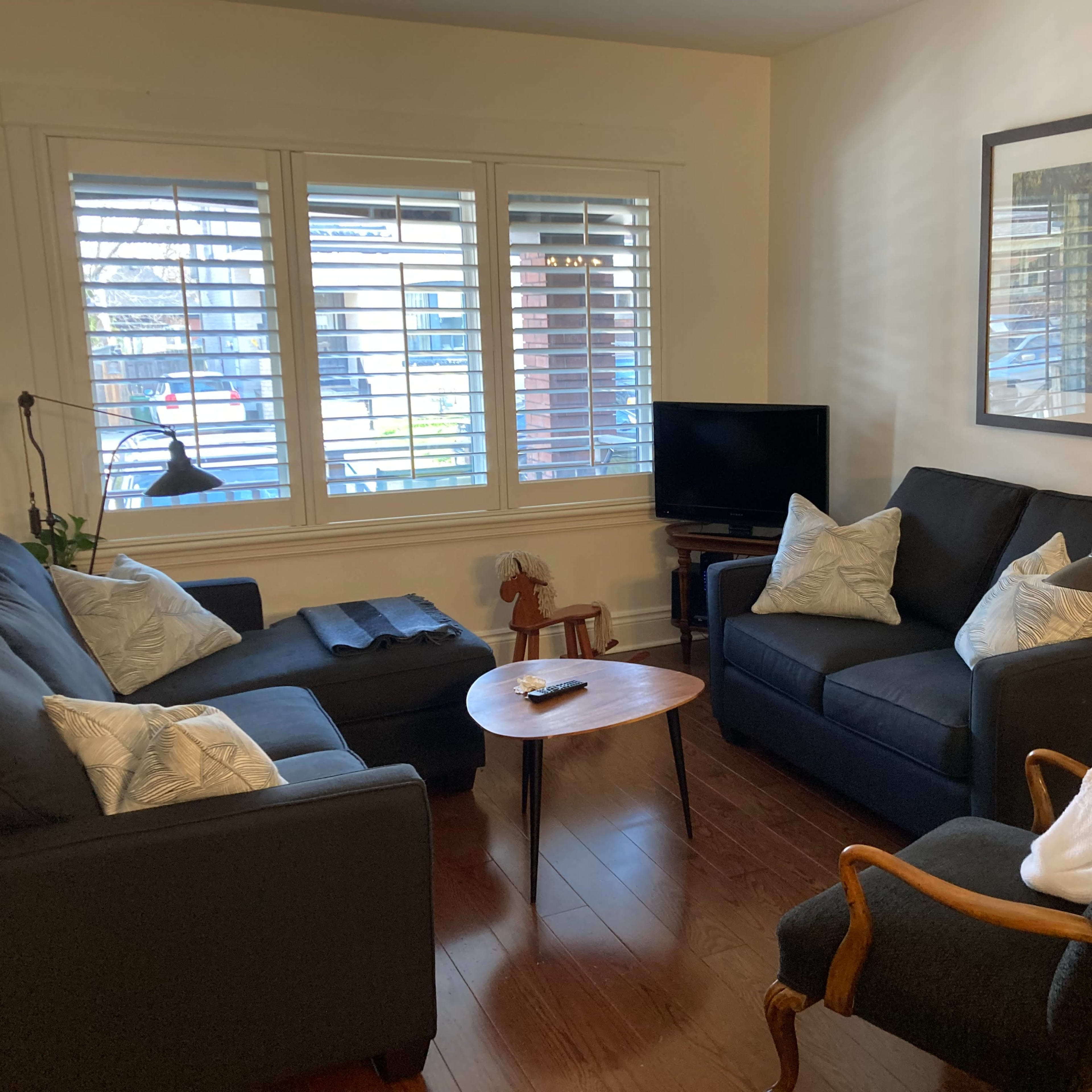 A small living room with two dark sofas, a wooden coffee table, a television, and a window with shutters.