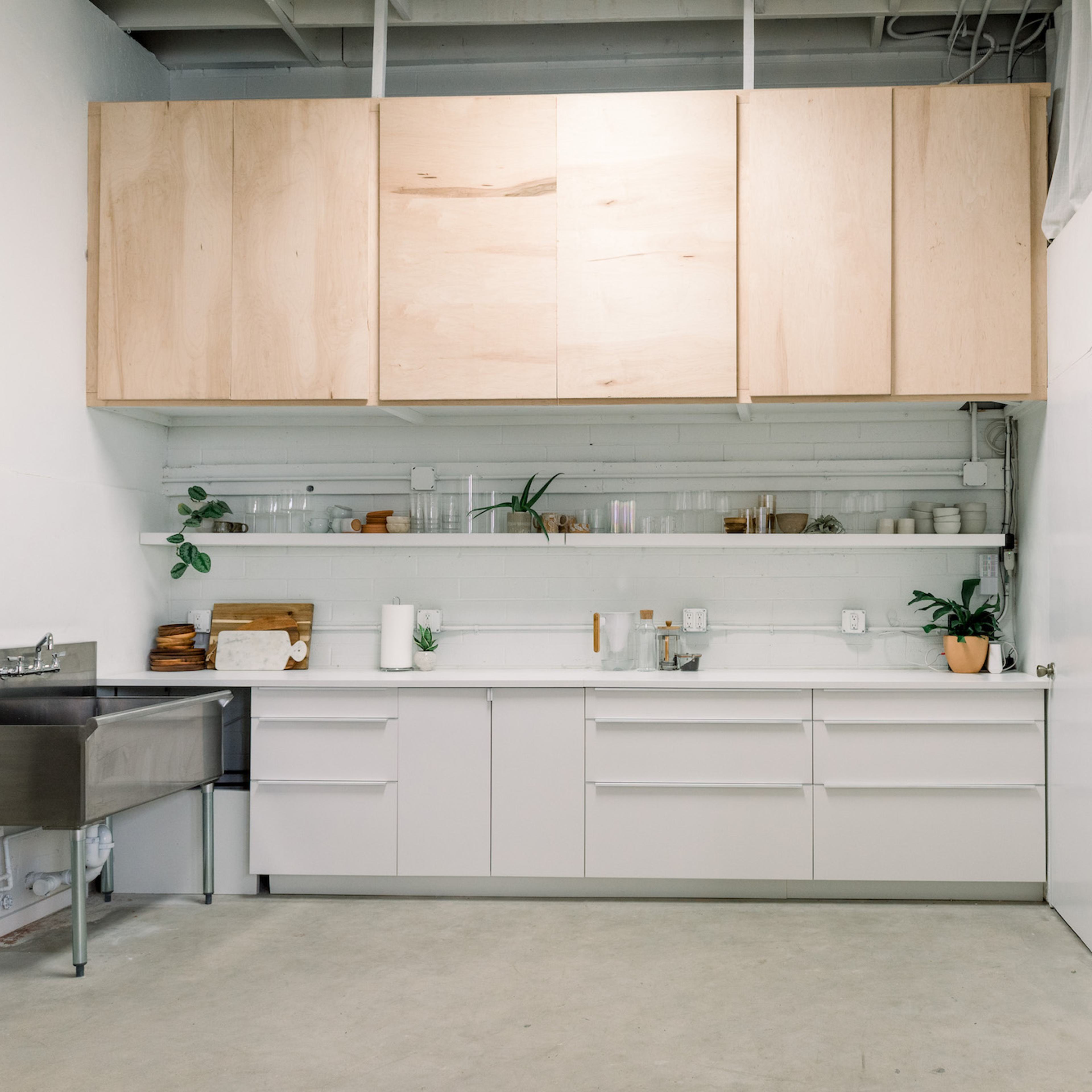 A modern kitchen with white cabinetry, wooden overhead cabinets, and minimal decor along the countertop.