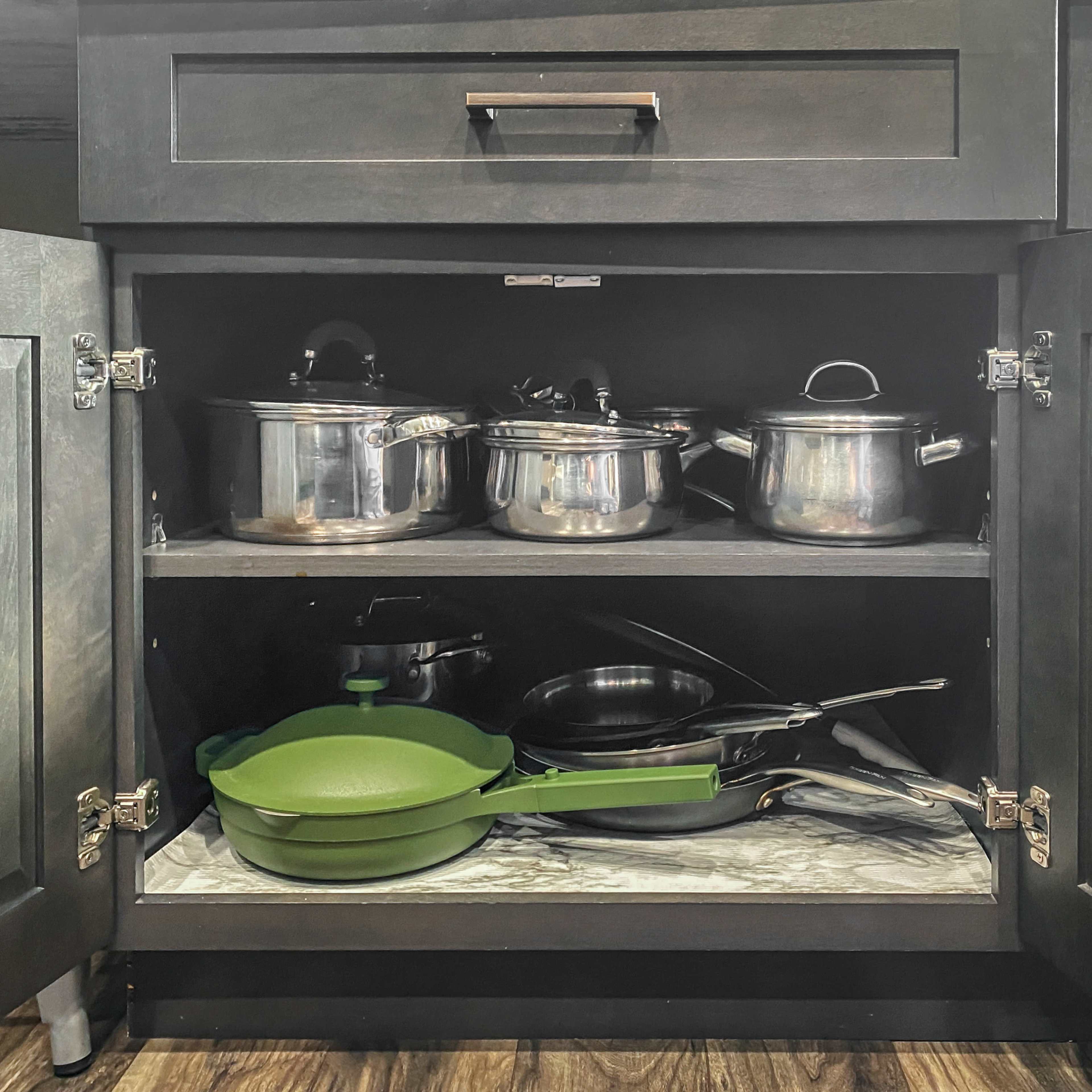 A variety of pots, pans, and cookware are neatly arranged on shelves inside a dark kitchen cabinet.