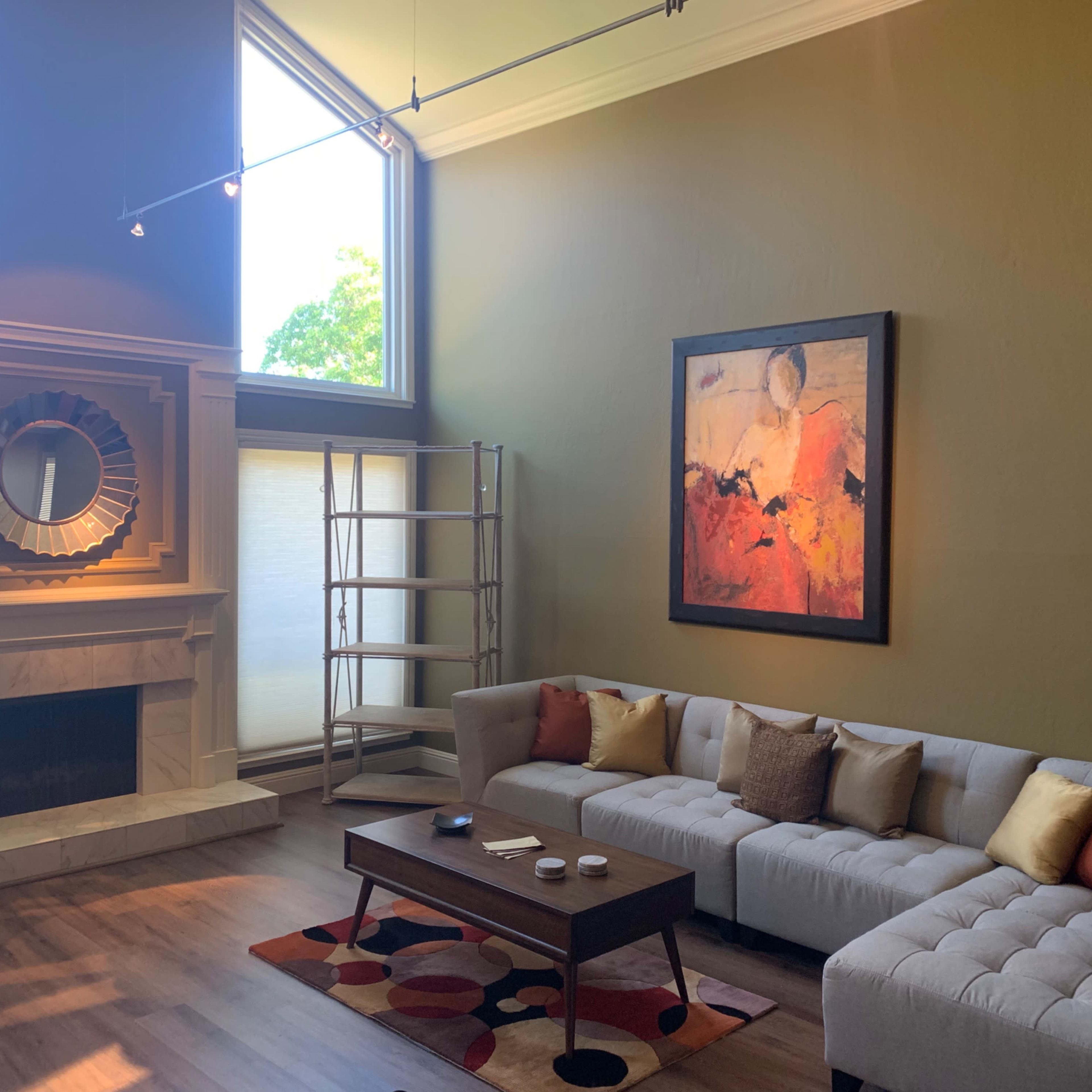 A modern living room featuring a light-colored sectional sofa, a wooden coffee table, a large abstract painting, and a fireplace.