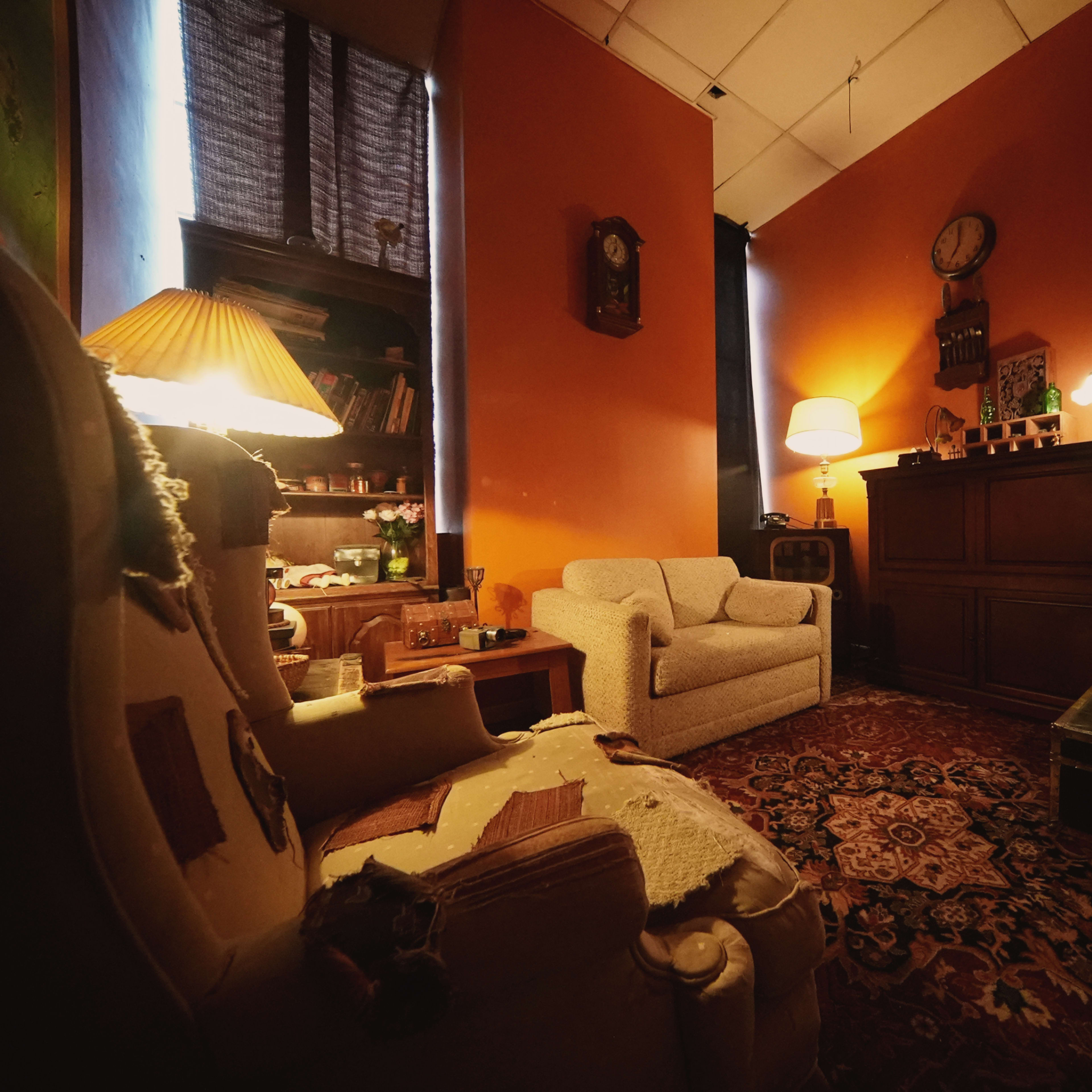 A cozy room with orange walls, furnished with a light sofa, a lamp, and various decorative items on shelves and tables.