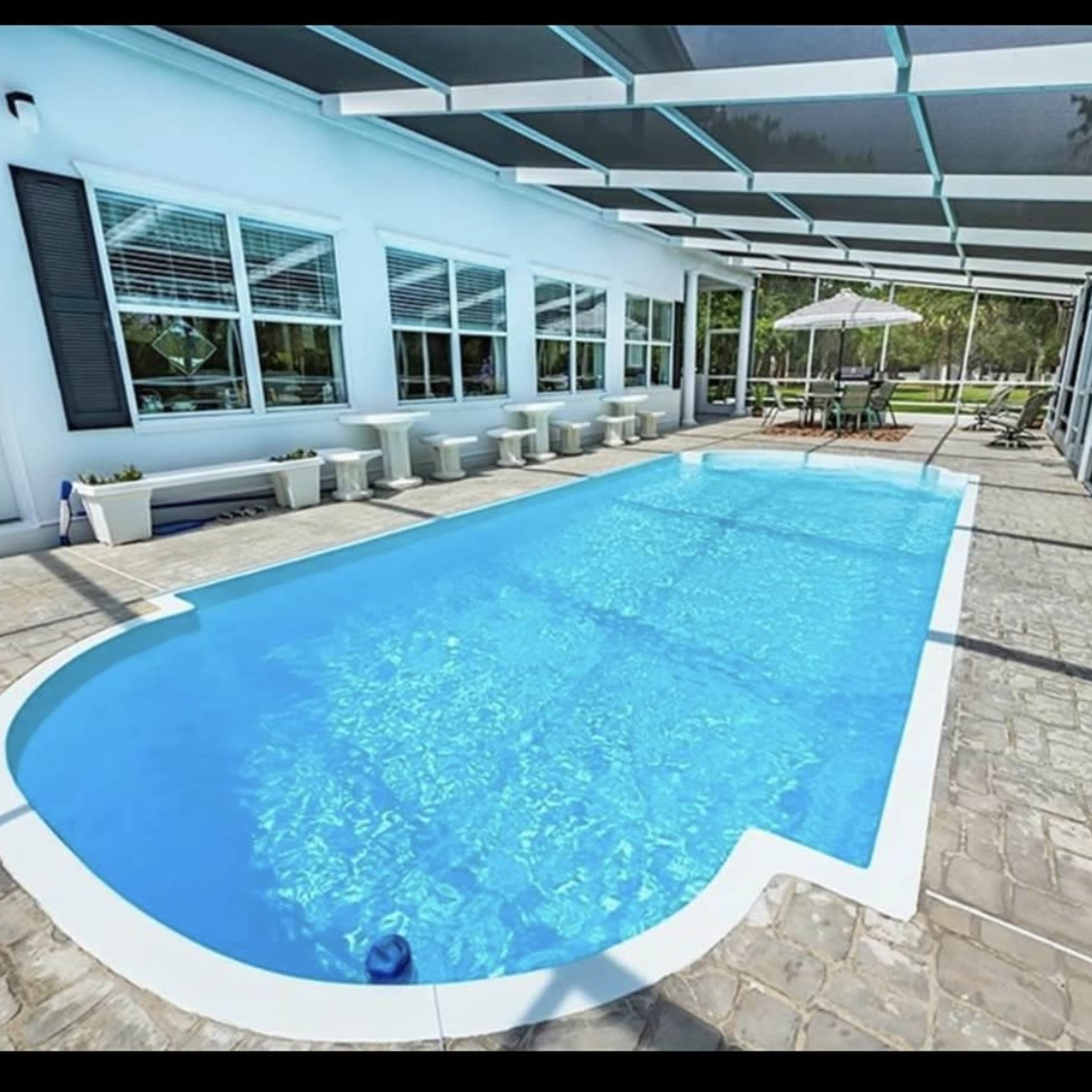 A rectangular swimming pool located in a screened-in patio area with white walls and a patio set beside it.