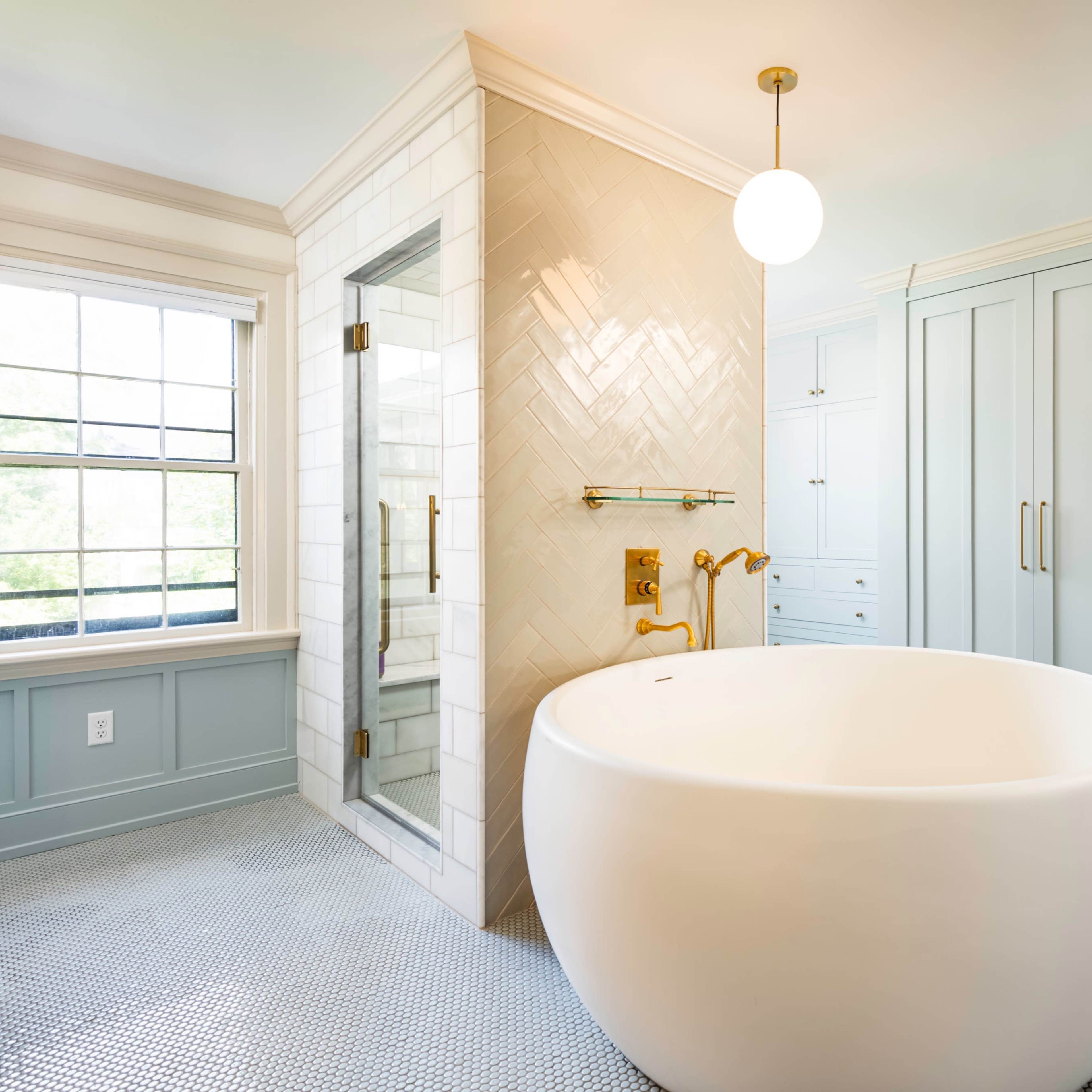 A modern bathroom featuring a freestanding oval bathtub, a glass shower enclosure, and cabinetry with a light blue finish.