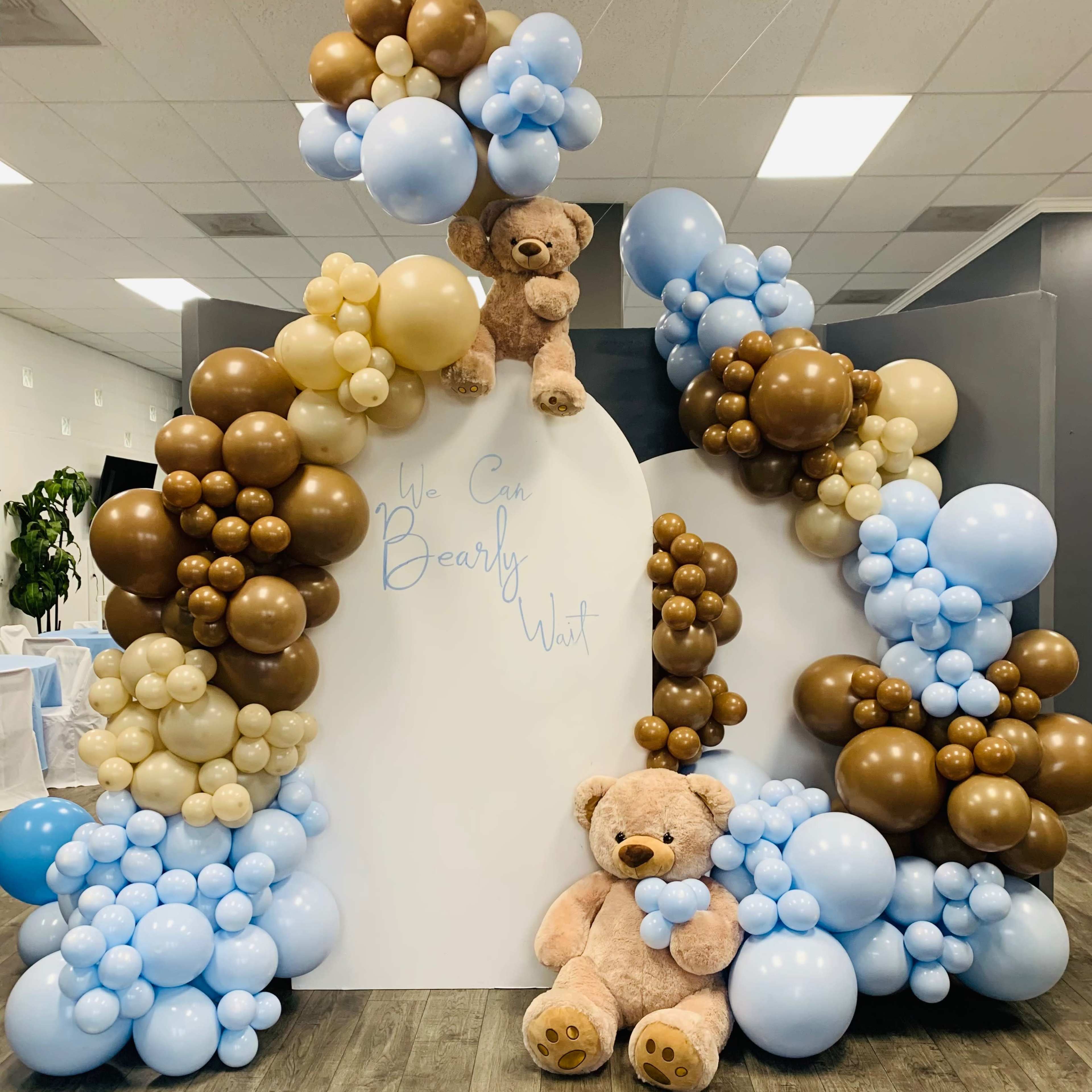 A decorative display featuring a large arrangement of balloons in various colors, including brown, cream, and light blue, along with two teddy bears positioned prominently at the center.